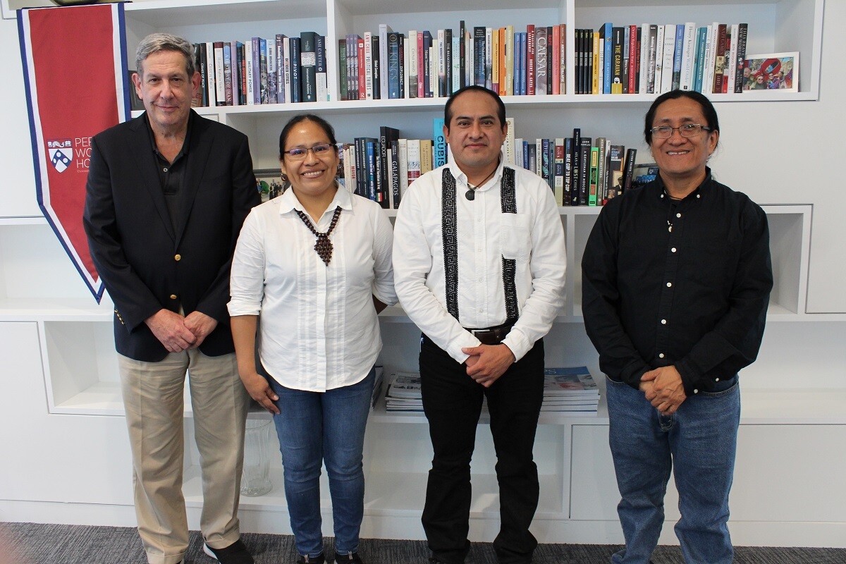 Four people stand in front of a white bookcase with a red vertical banner hanging from the image's left side