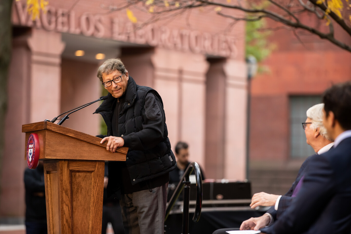 Stuart Weitzman at a podium turning to look at the others sitting on the stage 