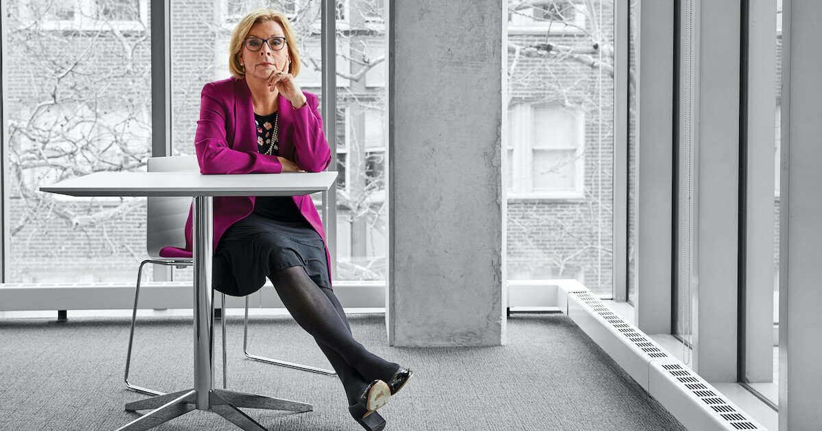 Marci Hamilton sits at a table beside large windows overlooking Penn campus.