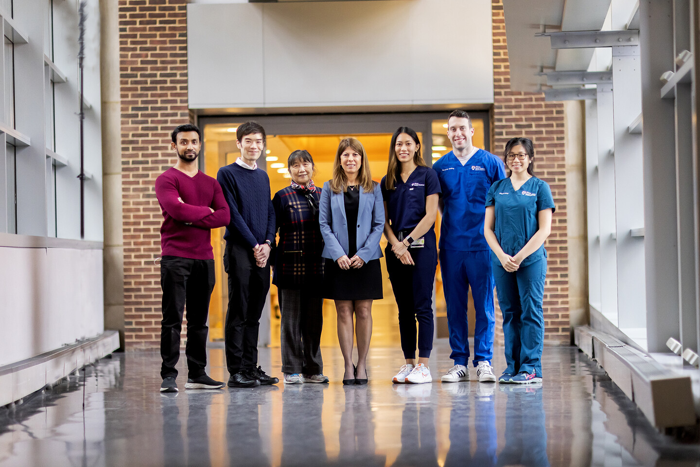 Group of seven scientists stand in a window-lined hallway
