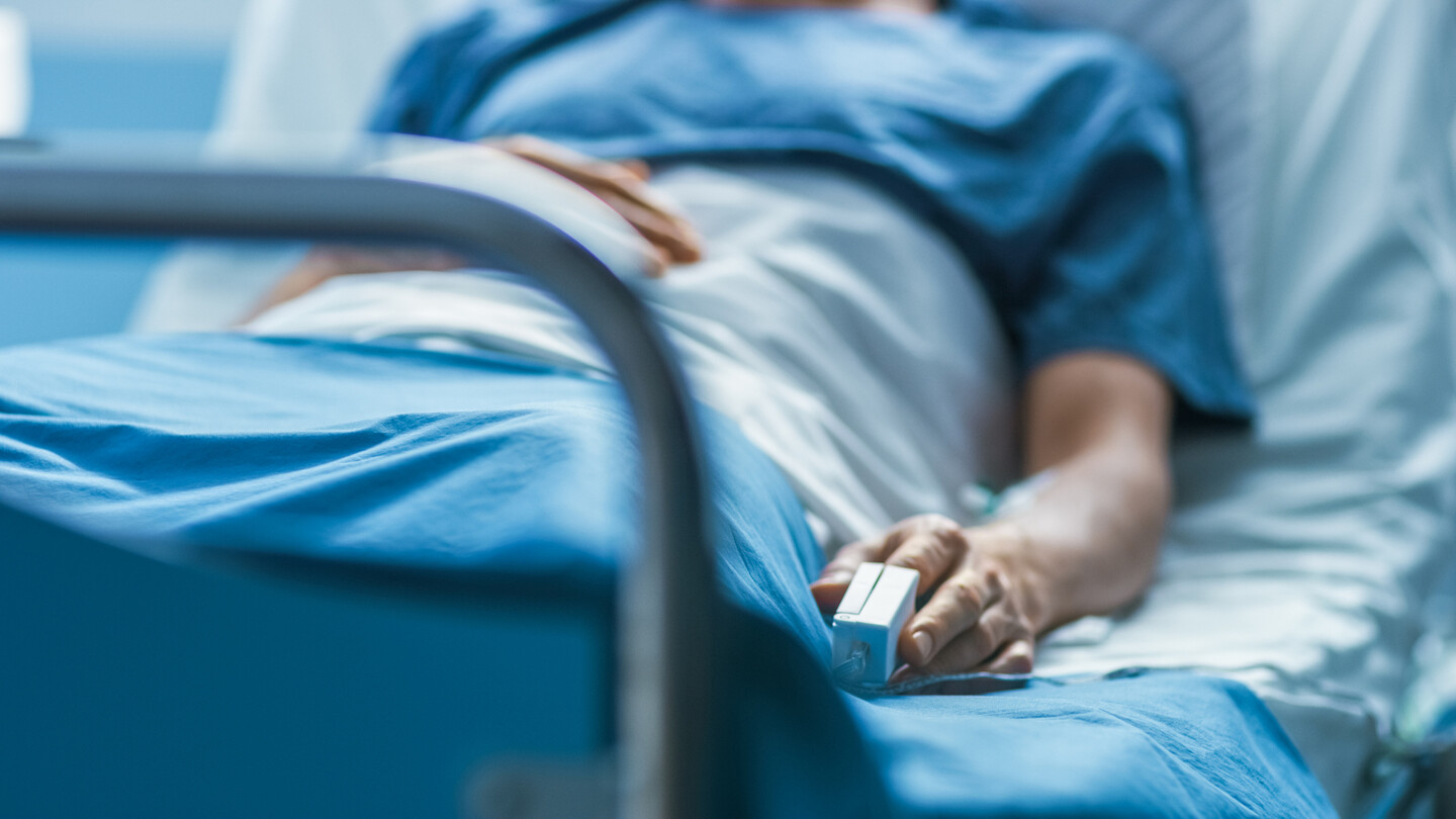 Image of a person laying in a hospital bed, with a pulse oximeter on their finger.