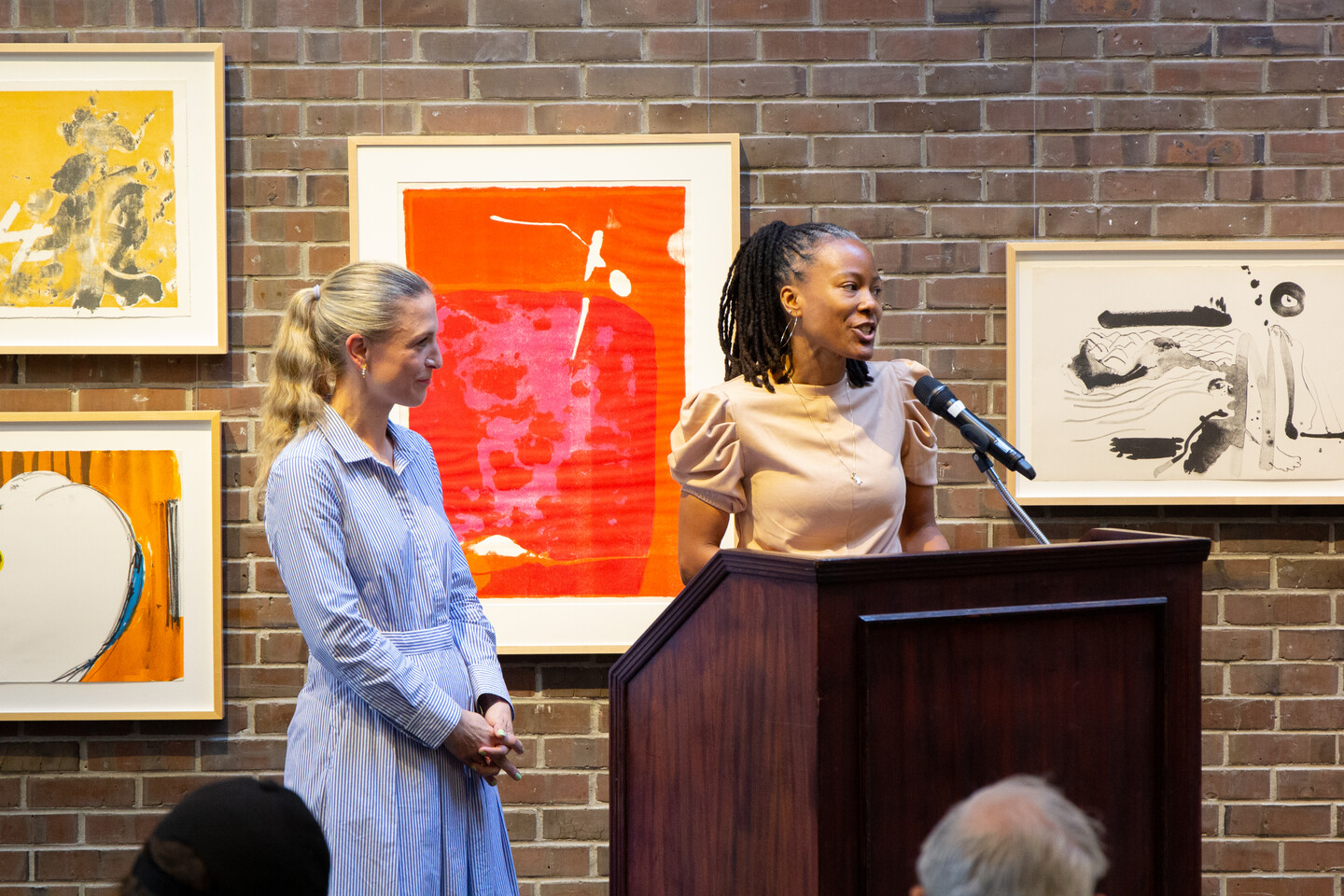 Two speakers at a podium with artwork behind them. 