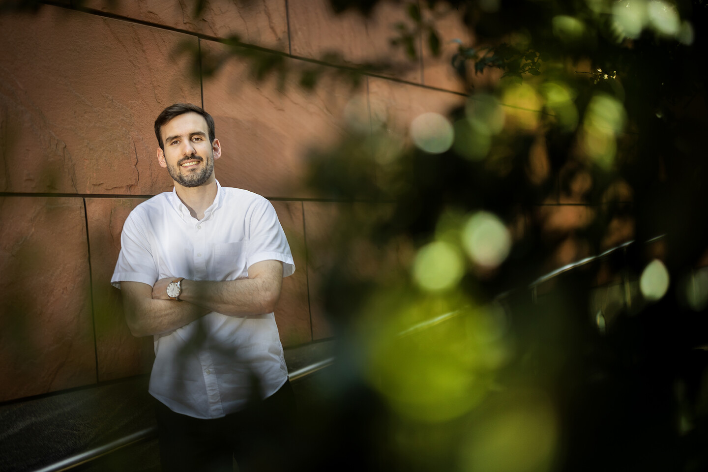 Nick Martin stands against a red sandstone building, with foliage in the foreground