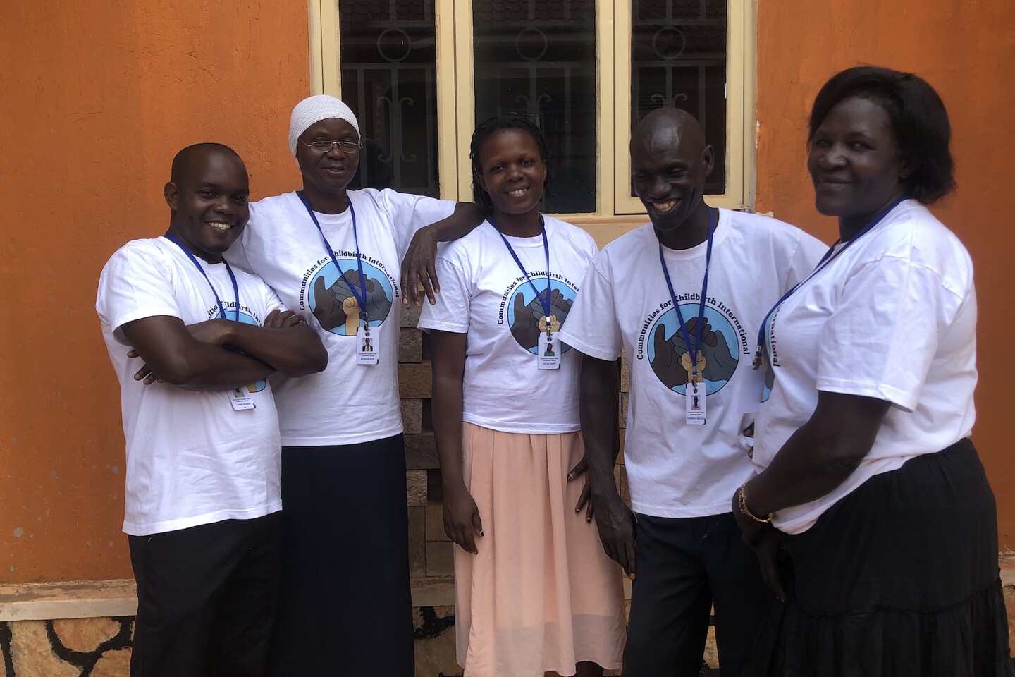 Five people wearing "Communities for Childbirth" t-shirts in front of a burnt orange stucco building