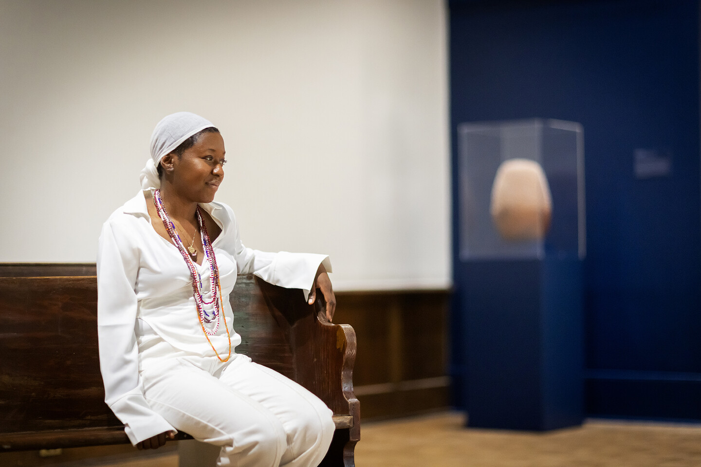 artist sitting on wooden pew with ceramic work in glass case behind 