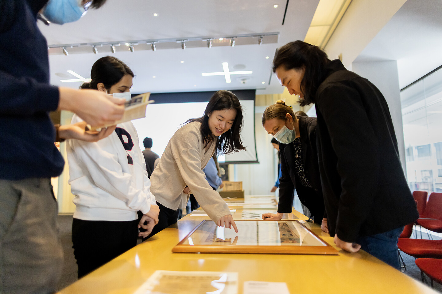 five students standing next to table looking at printed materials with professor