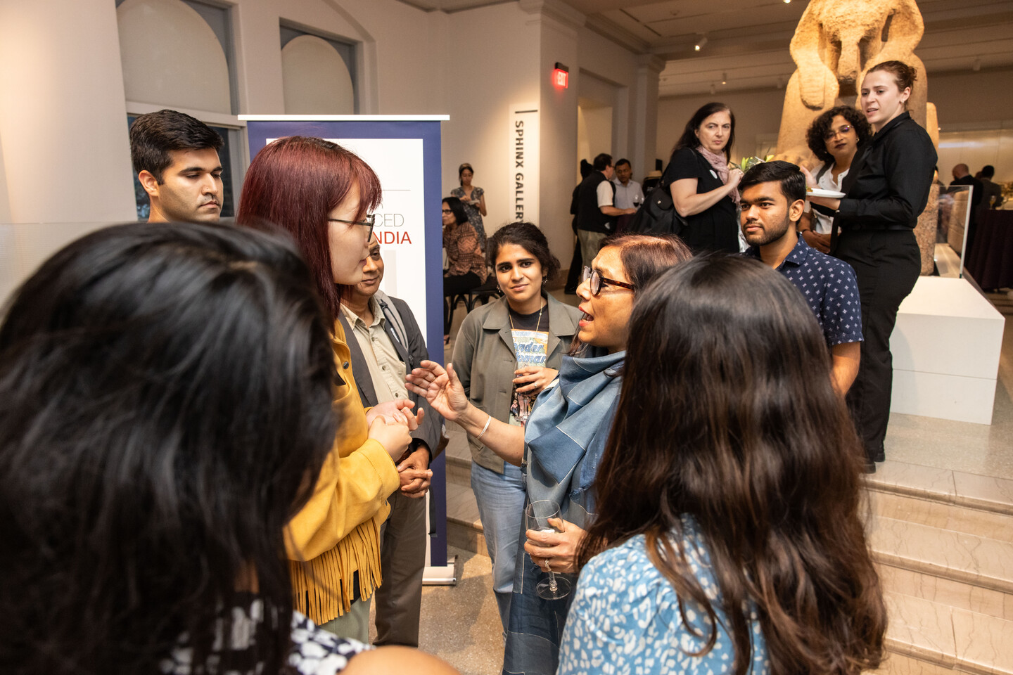 A group of people cluster around Mira Nair at the Penn Museum with the Sphinx in the background.  