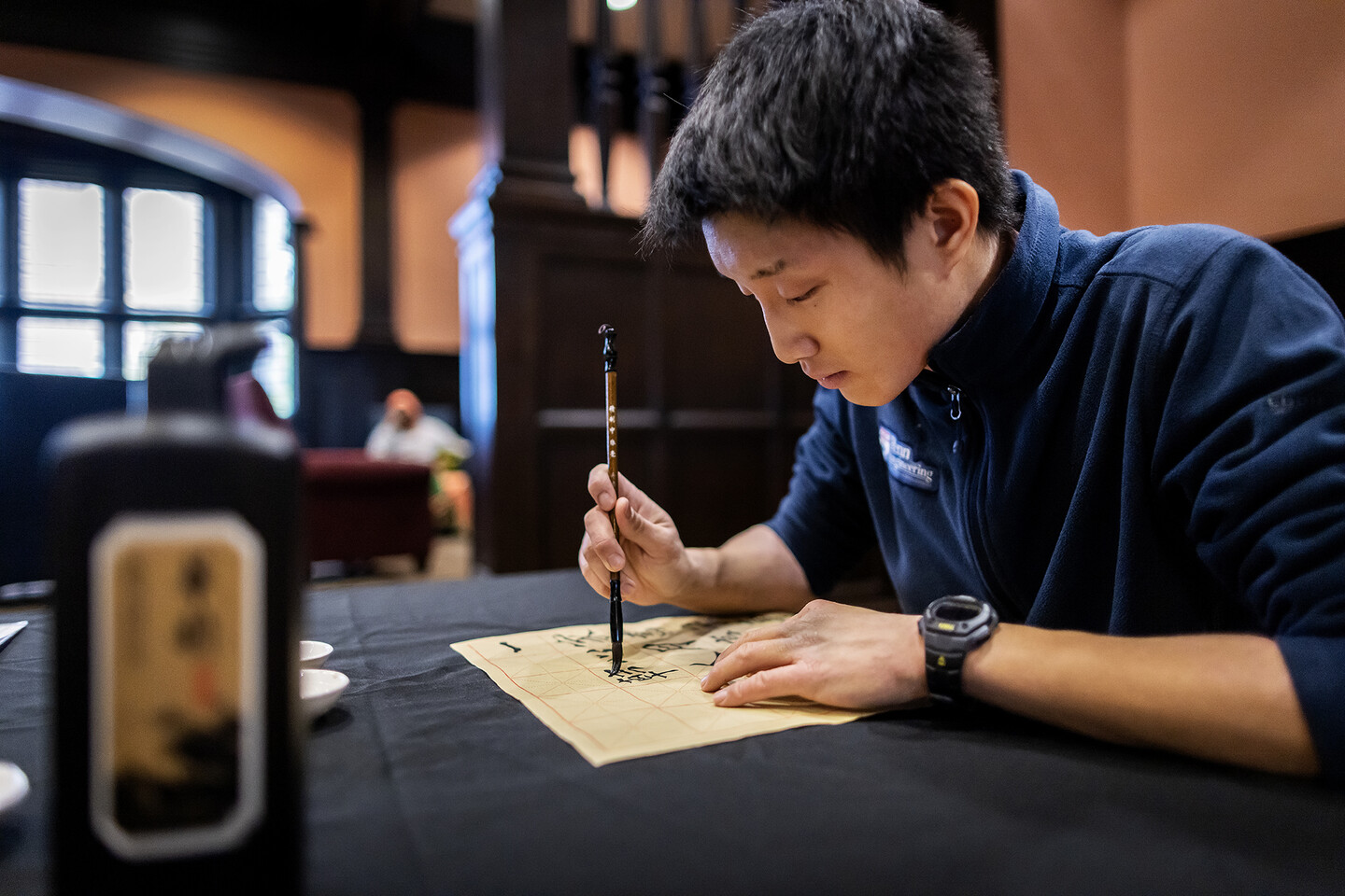 Alan Han carefully stroking a piece of paper with a calligraphy brush.