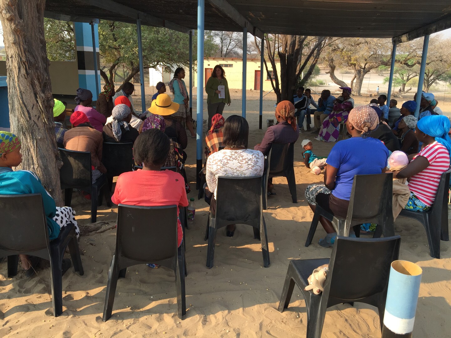 People sit on chairs surrounding two individuals standing and explaining a study.