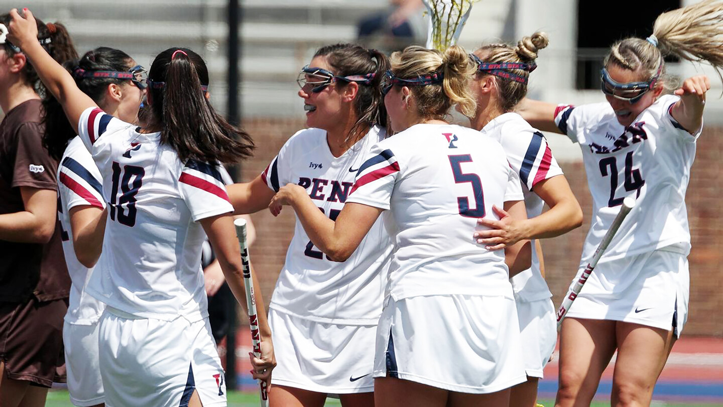 Members of the women's lacrosse team celebrate in a circle.