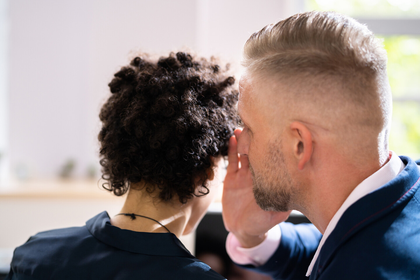 One person whispers in the ear of another.
