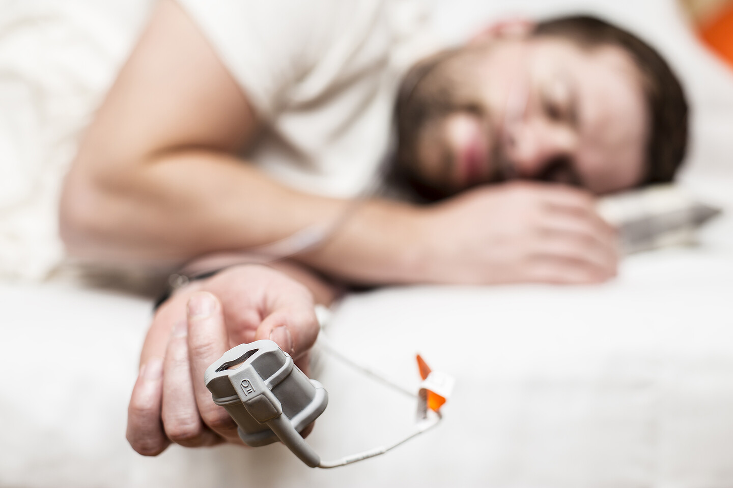 A person laying in bed with a sleep apnea tracker on their finger.