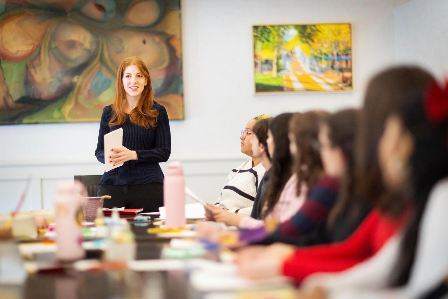 A teacher standing at the head of a table speaking to students.