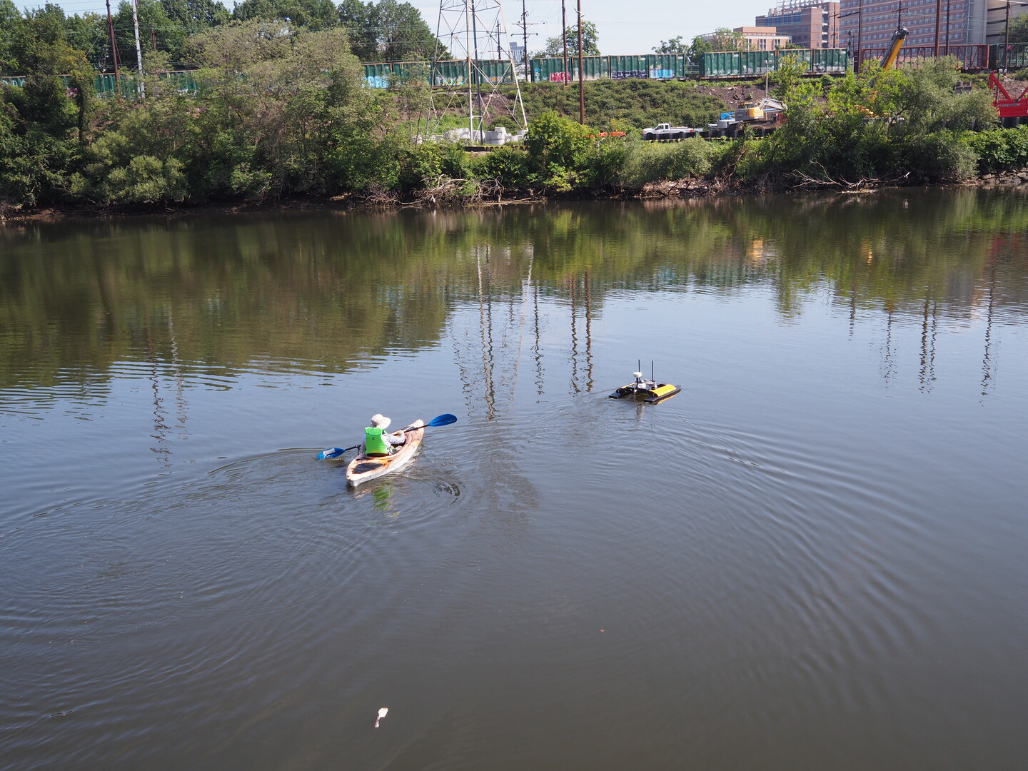 Person in a kayak wades through the Schuykill river near an autonomous swimming-robot.
