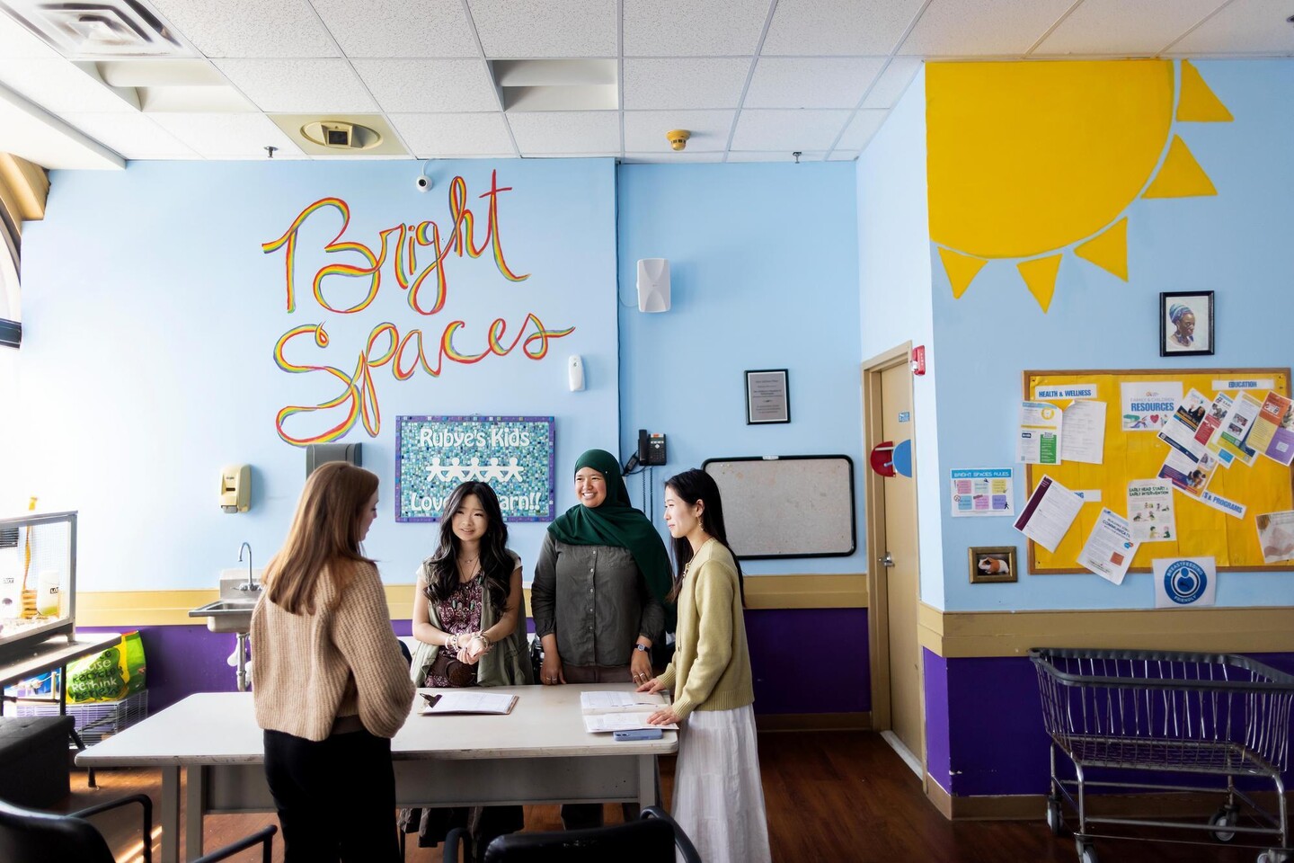 Four people gathered around a table inside a bright and cheerful room that has a 'Bright Spaces' mural on its back wall.