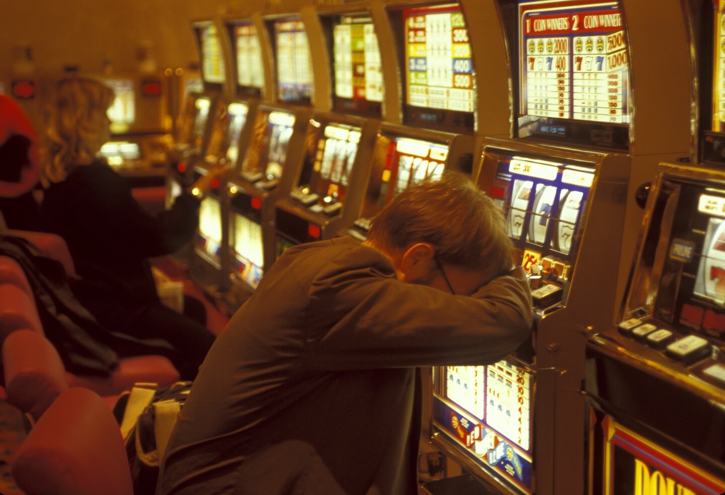 A person rests their head on a slot machine in a casino