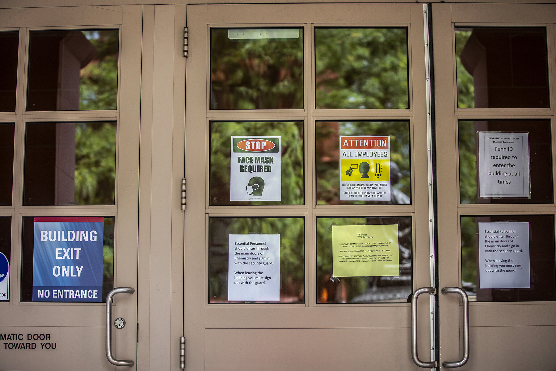 Multiple signs posted on a door regarding COVID precautions that read STOP FACE MASK REQUIRED among other messages.