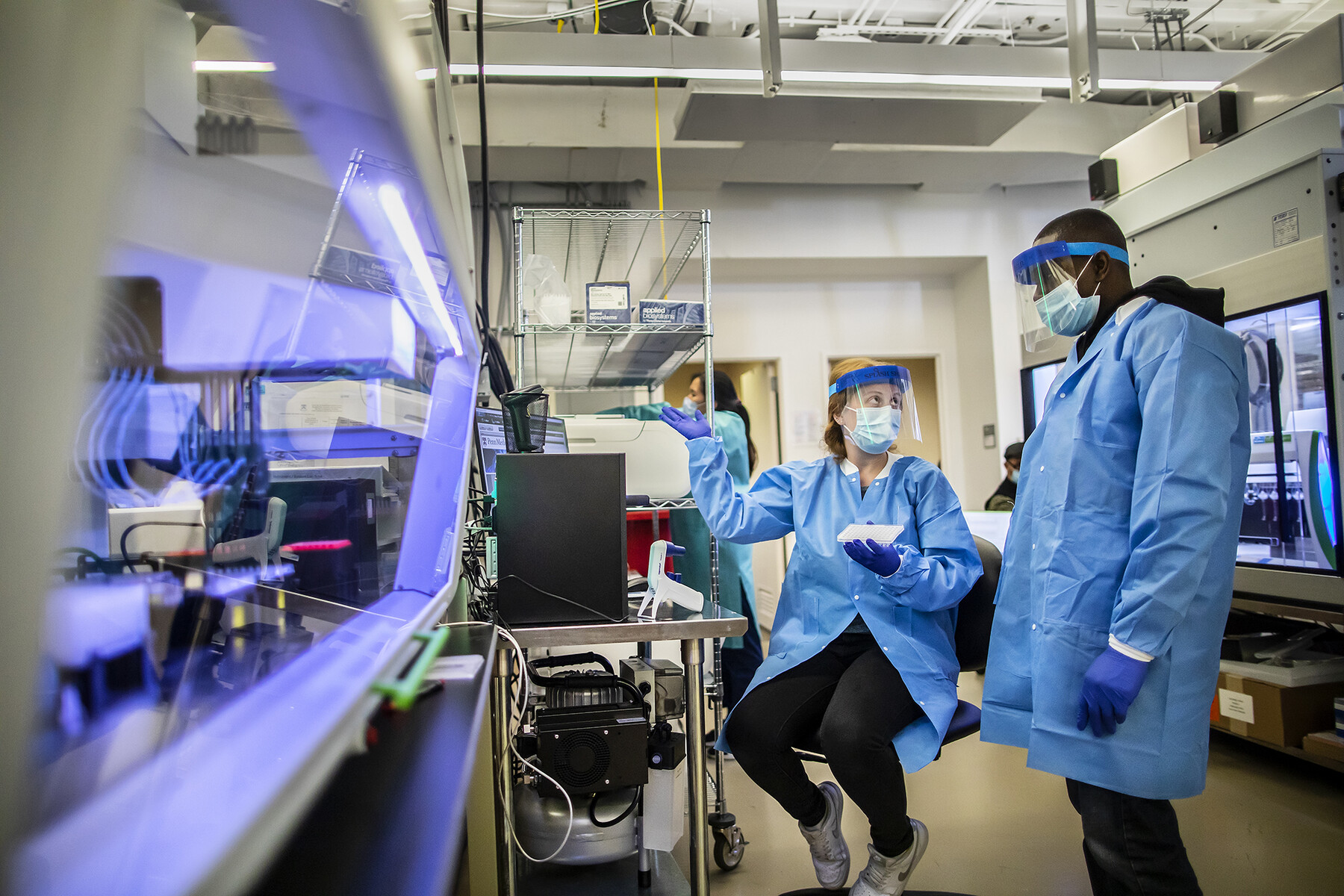 Two people in full PPE, one seated, on standing, in a lab on campus.