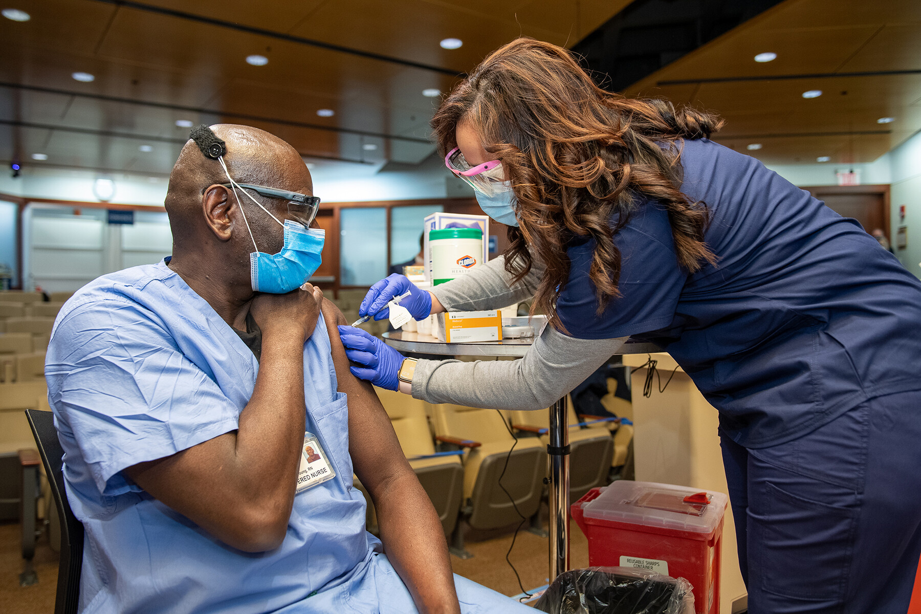 Penn medical worker wearing a face mask receives the COVID vaccine in their upper arm, administered by another masked hospital employee.