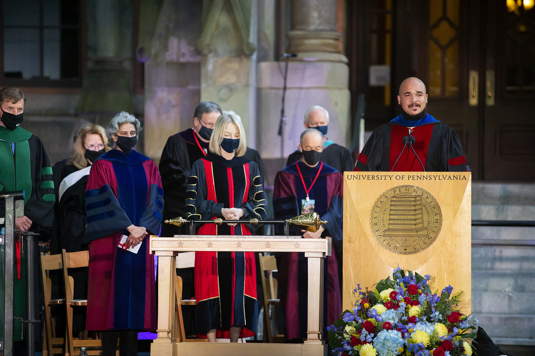 Chaz Howard speaks at a podium with Penn faculty behind him during Convocation in front of the steps of College Hall.