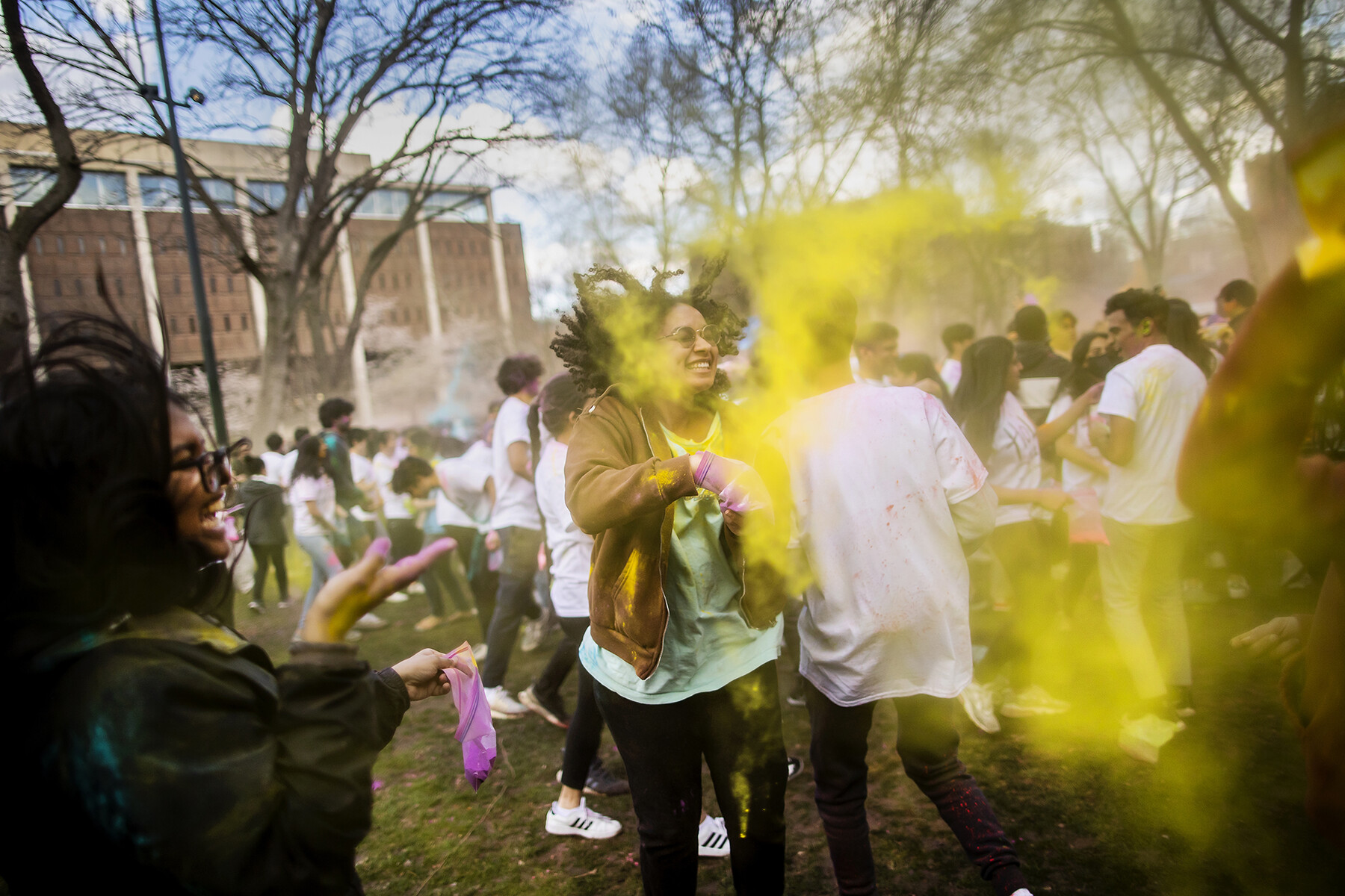 A crowd of people on College Green celebrating Holi with colorful powders.