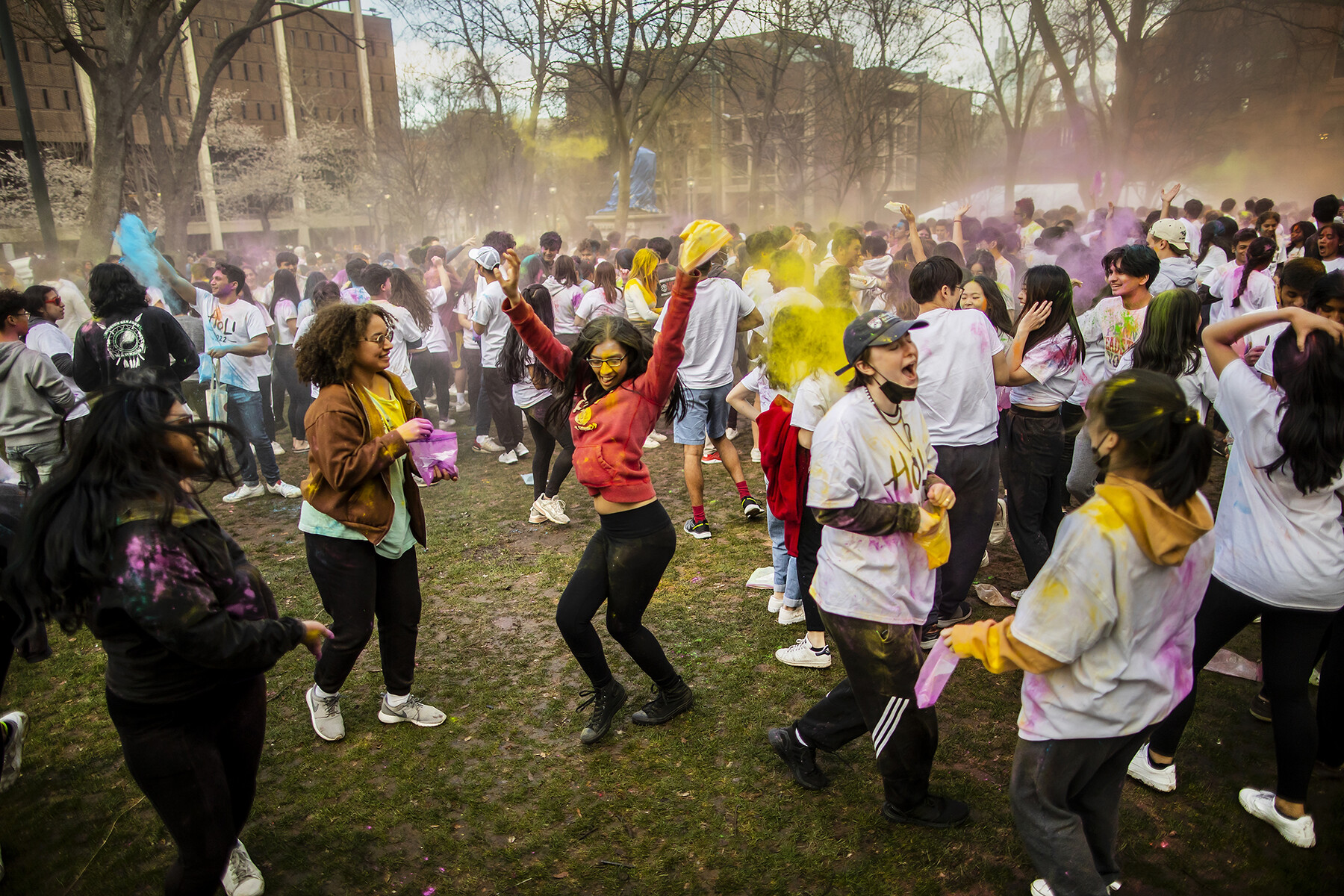 A crowd of people on College Green celebrating Holi with colorful powders.