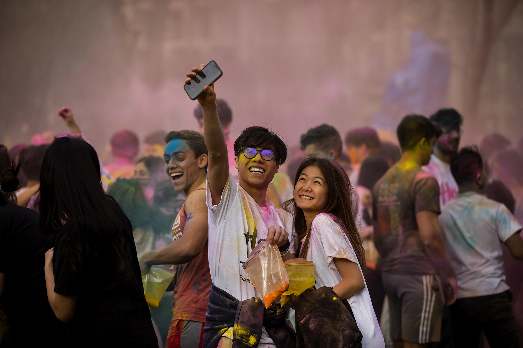 A crowd of people on College Green celebrating Holi with colorful powders.