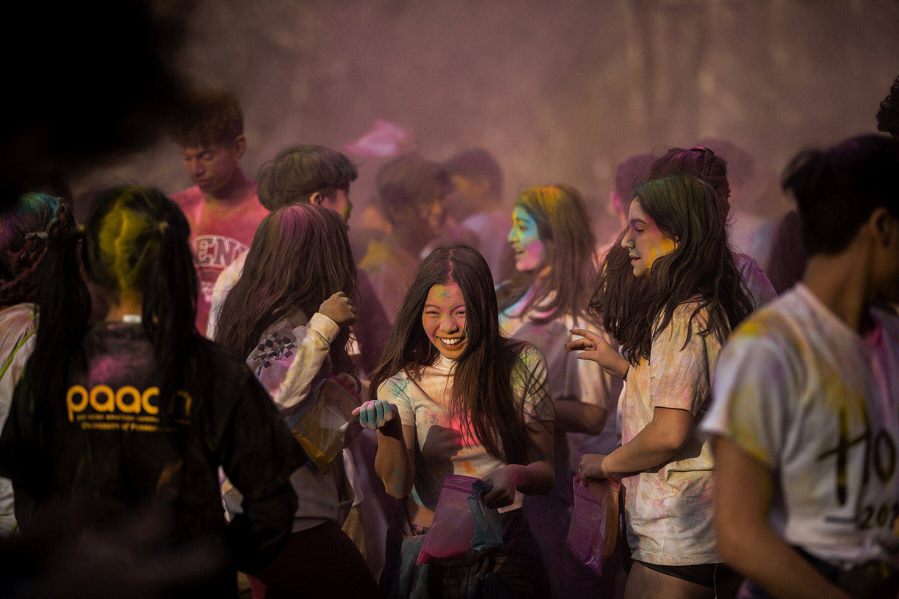 A crowd of people on College Green celebrating Holi with colorful powders.