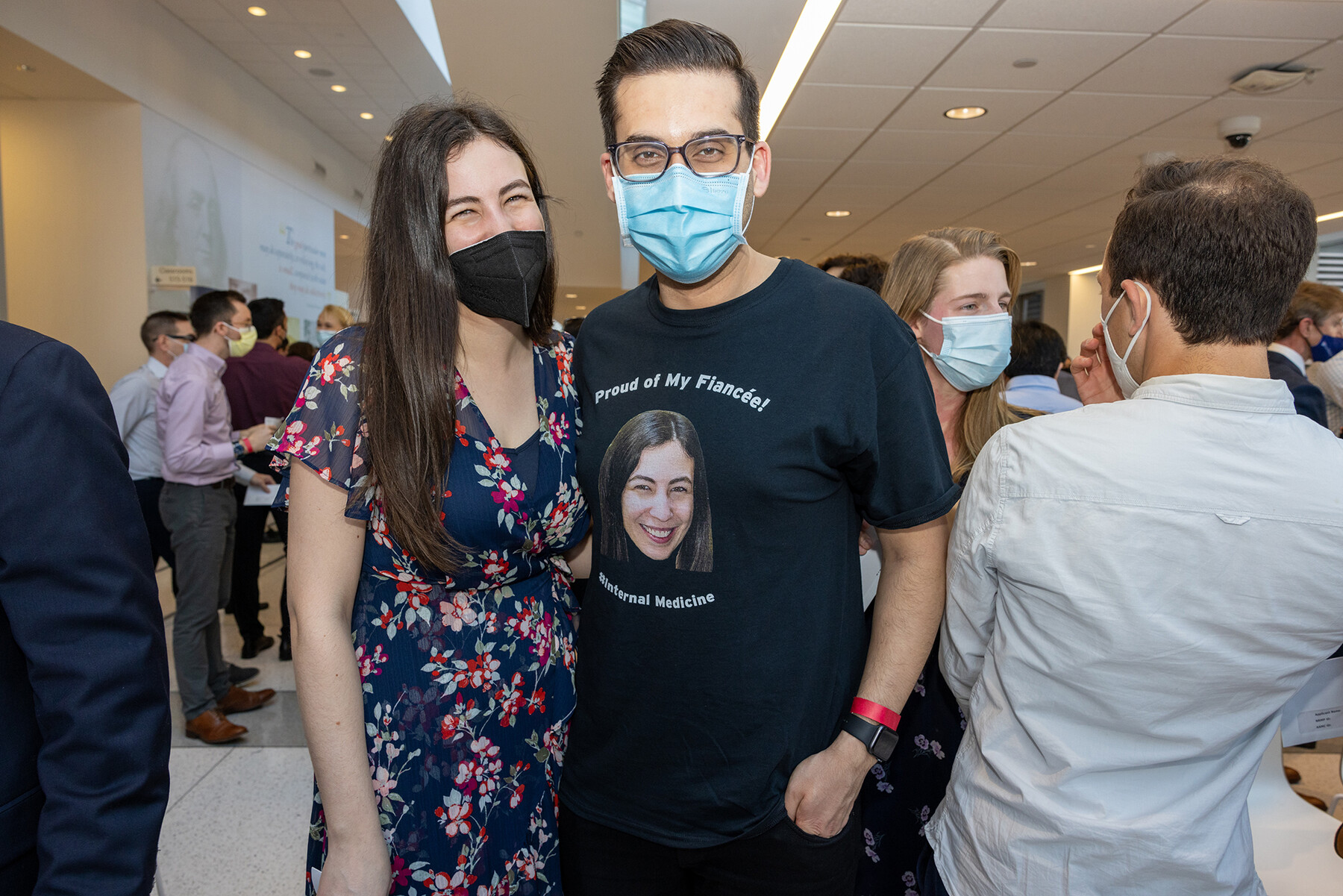 Two people smile on Match Day, one wears a shirt that reads Proud of My Fiancee with an image of them on the shirt.