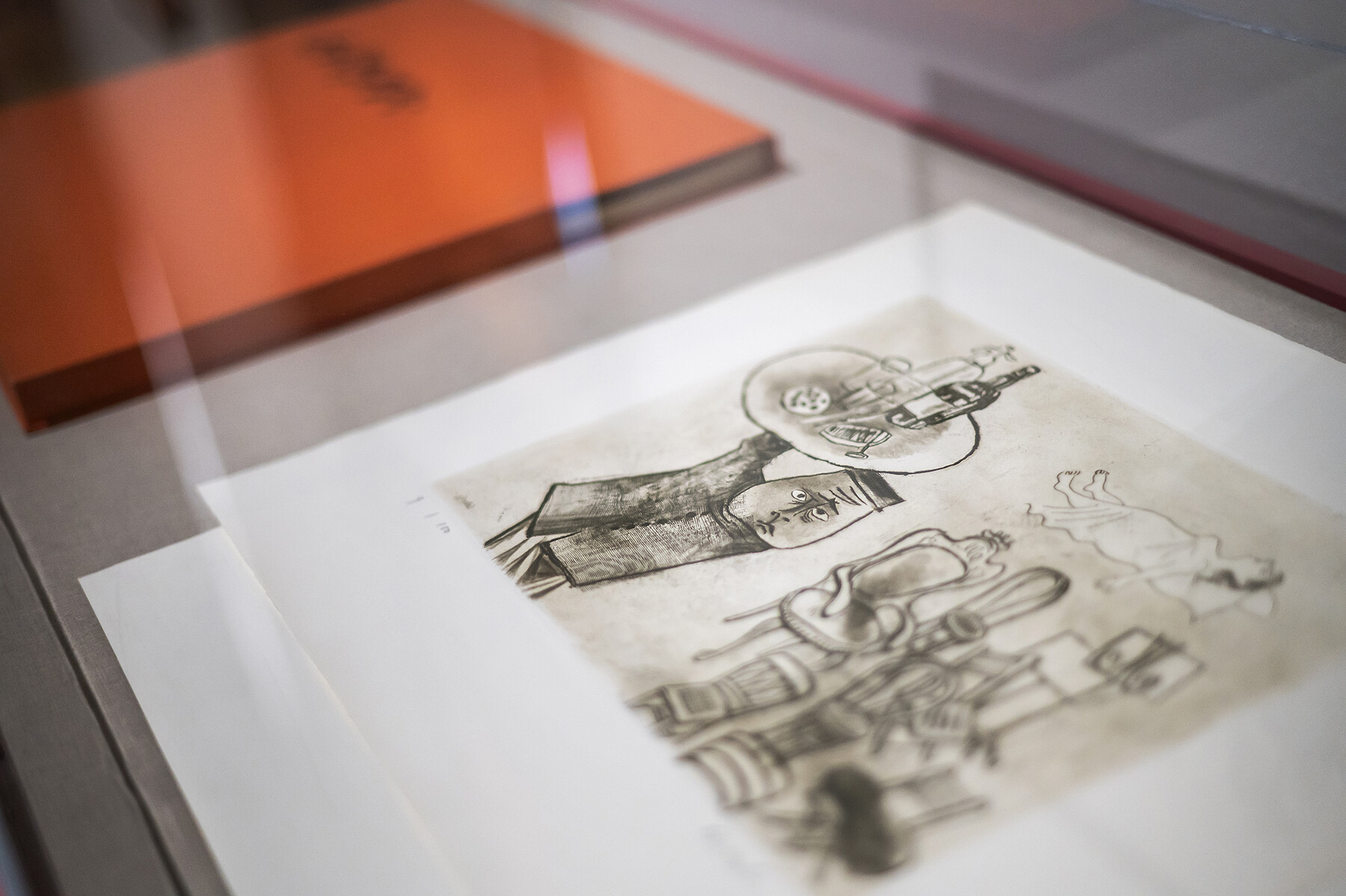 A charcoal drawing and a book underneath glass at the Arthur Ross Gallery.