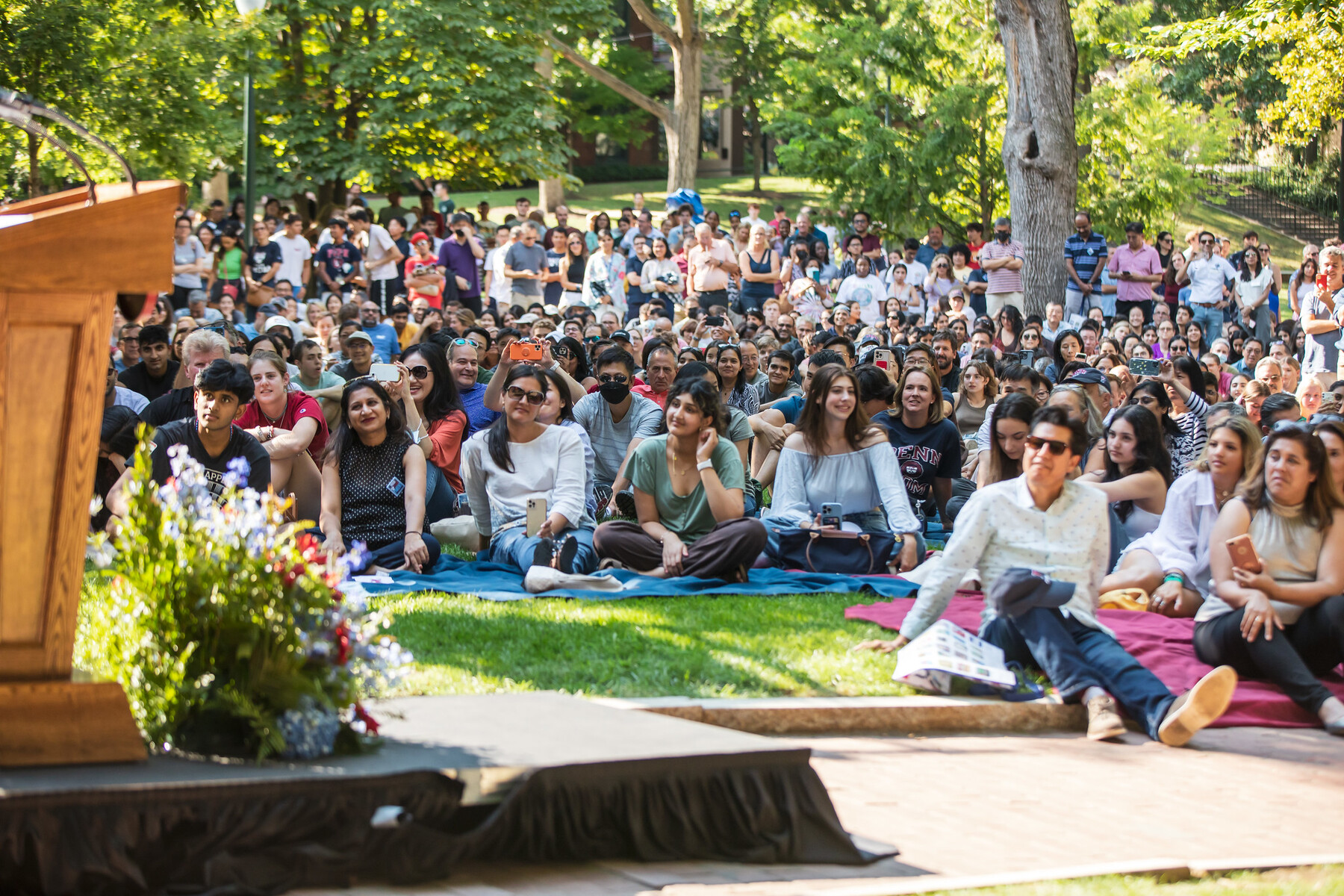A crowd of students and parents sitting on the lawn of College Green.