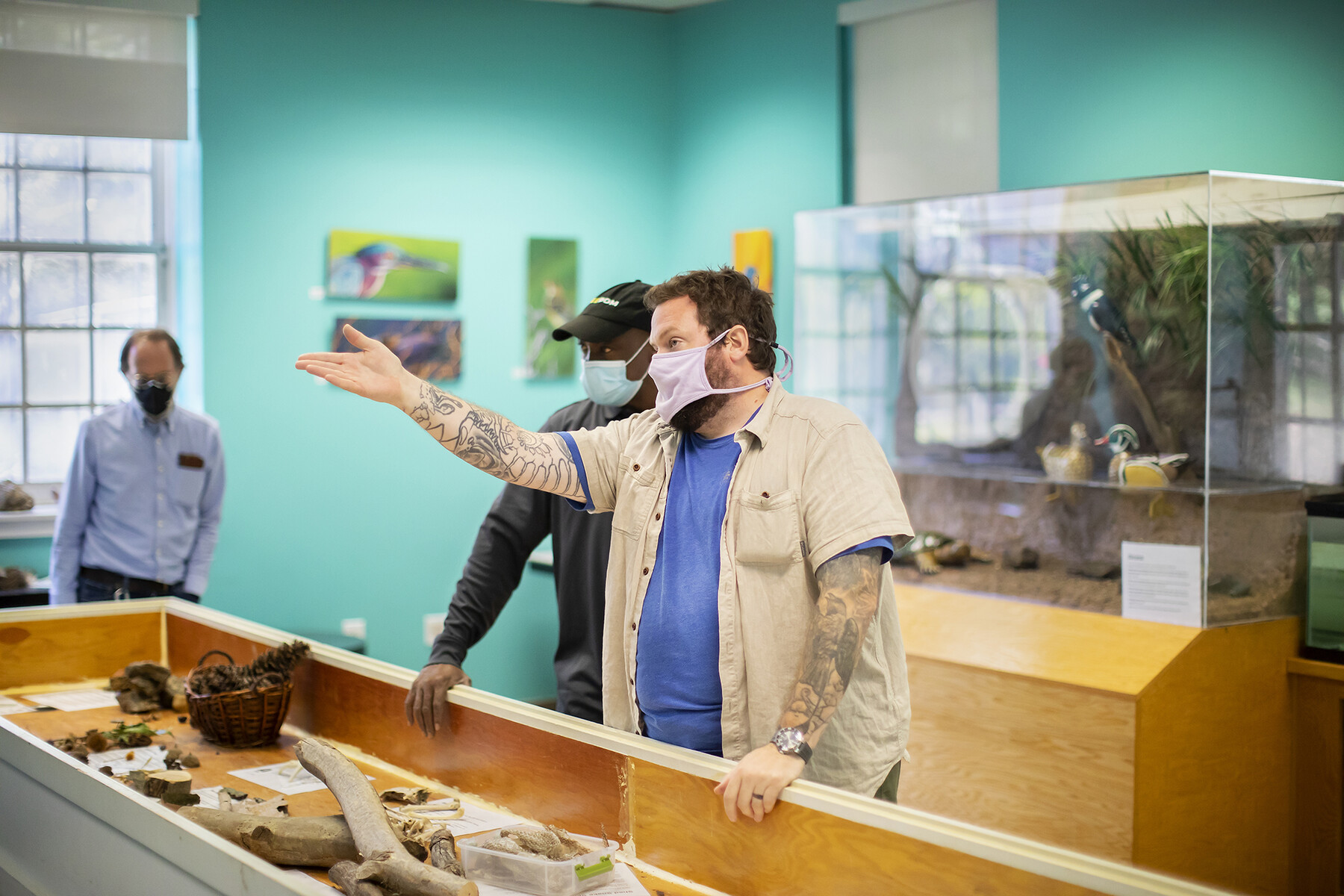 A person gestures in front of a classroom with an array of tree branchs, bark and other forest detritus in a large box on front of them.