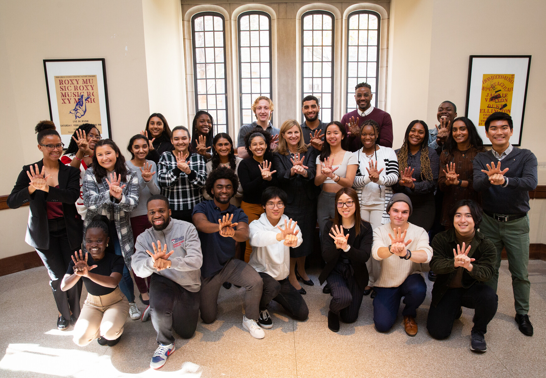 Liz Magill and a group of people posing for the camera doing a hand signal.