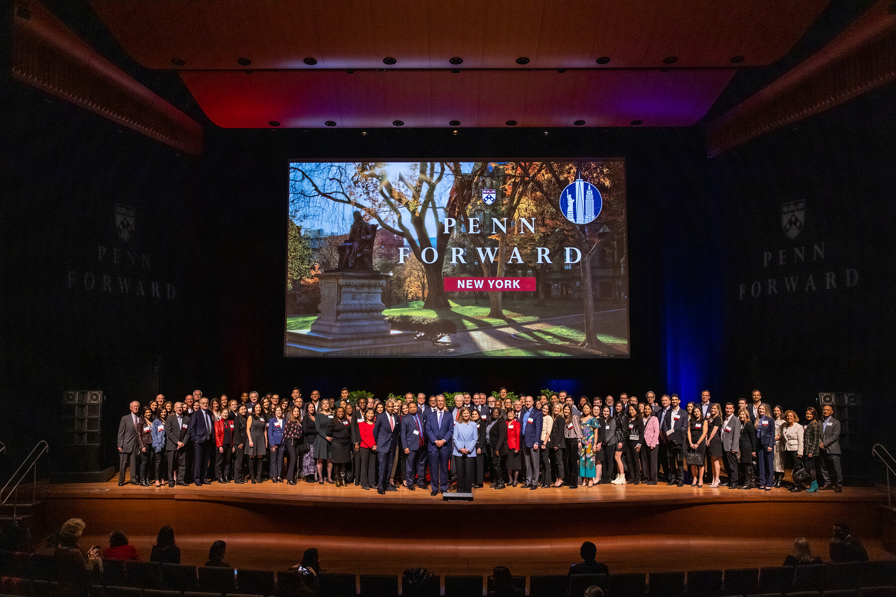A group of Penn alumni on stage with Penn Forward New York on screen behind them.
