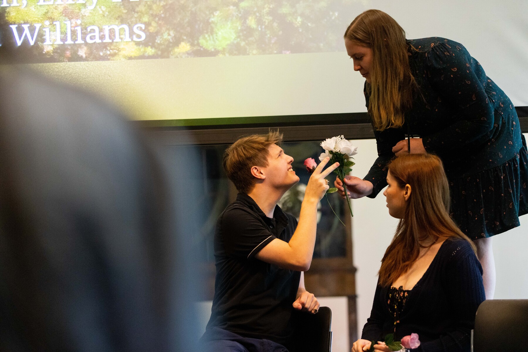 three students performing, one handing another a few flowers