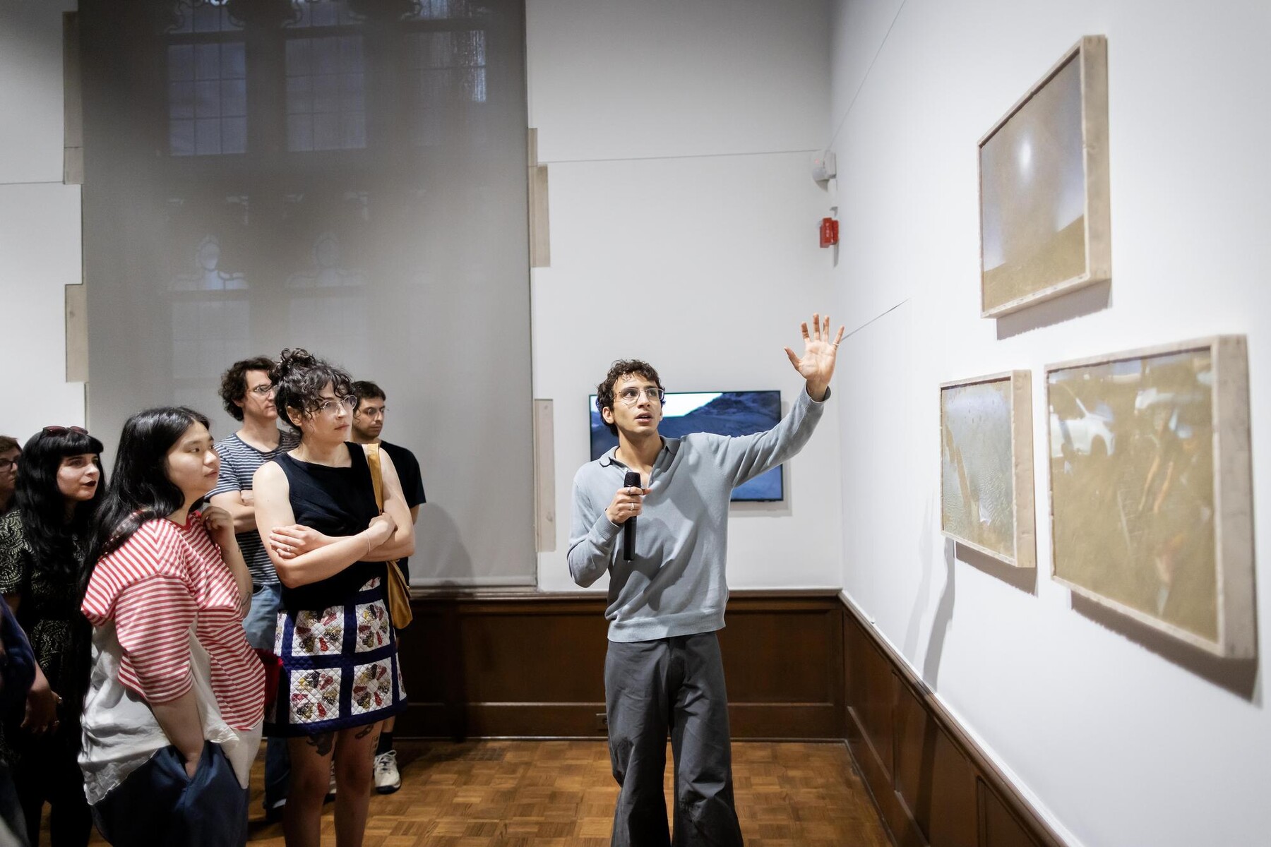 Eissa Attar speaking and gesturing to artworks with crowd listening