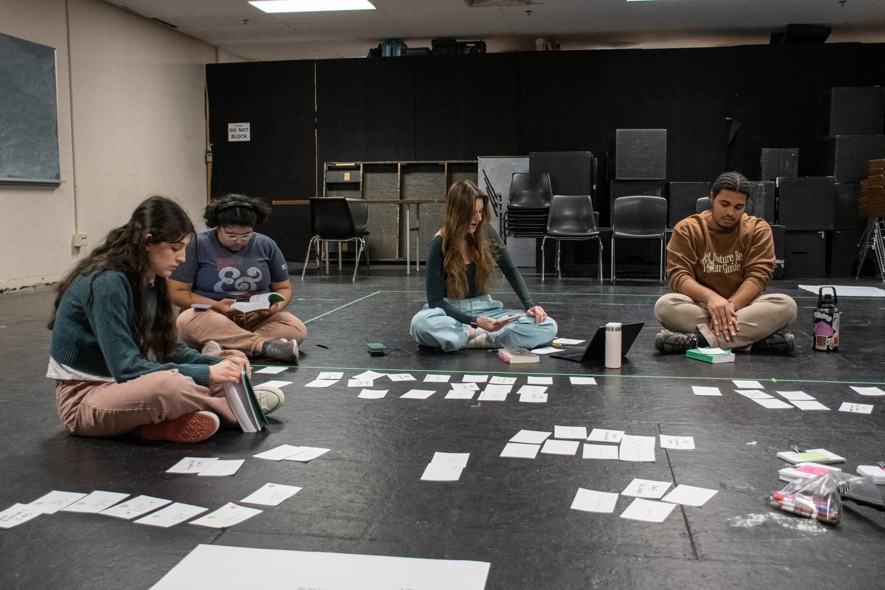 Anya Rothman, Beatriz Penzo-Mendez, Pandora Schoen, and Elliot Ross-Dick sitting on the floor of a classroom, surrounded by index cards.