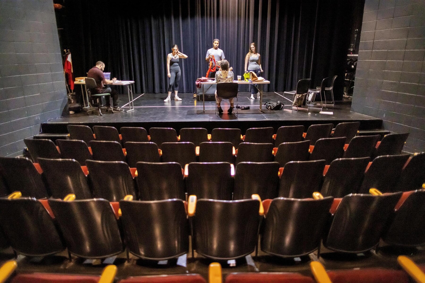 A foreground view of empty rows of audience chairs with Noah Levine, Anya Rothman, Elliot Ross-Dick, Pandora Schoen, and Margit Edwards.