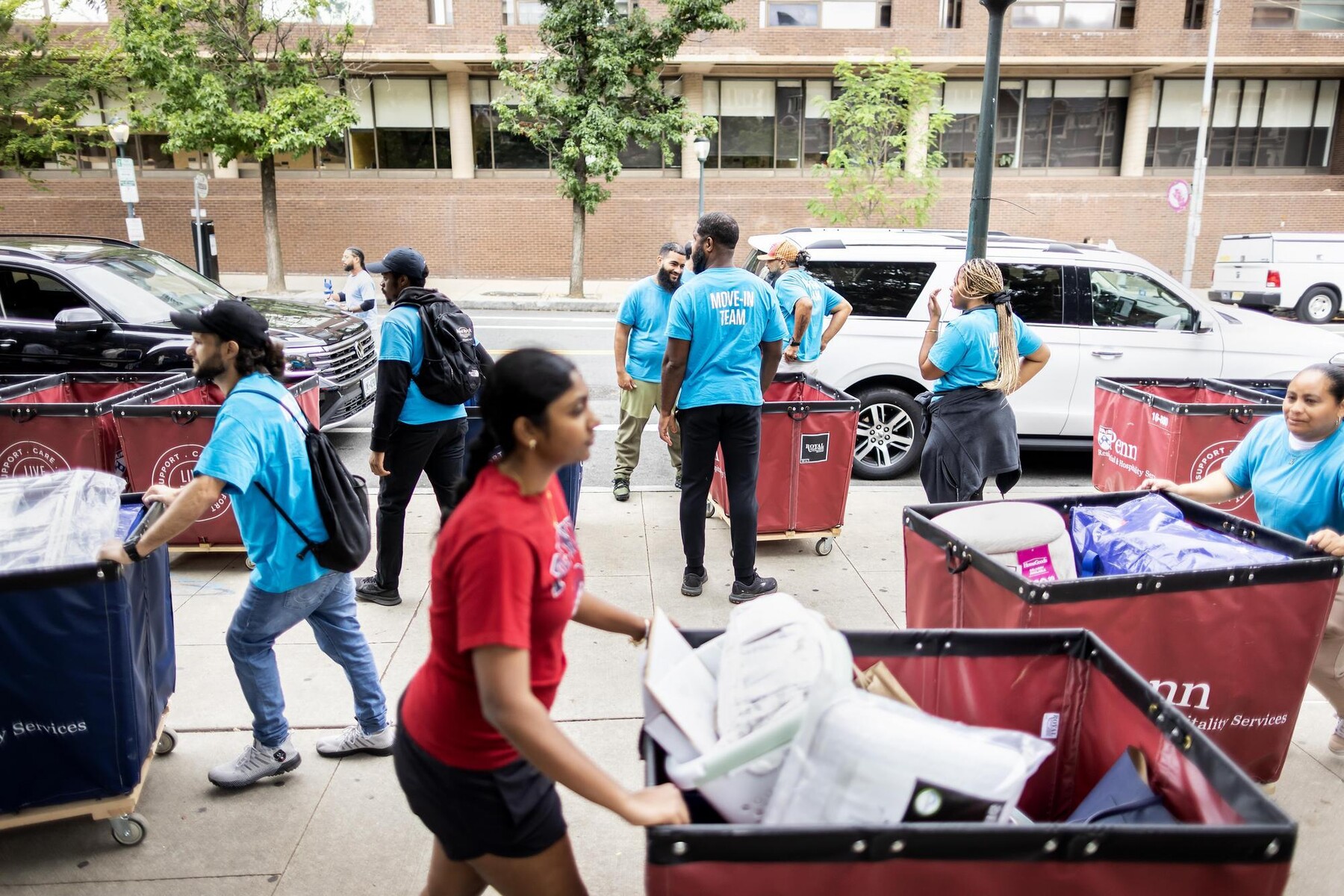 Move-In Team volunteers on Spruce Street pushing carts of move-in items unloaded from cars.