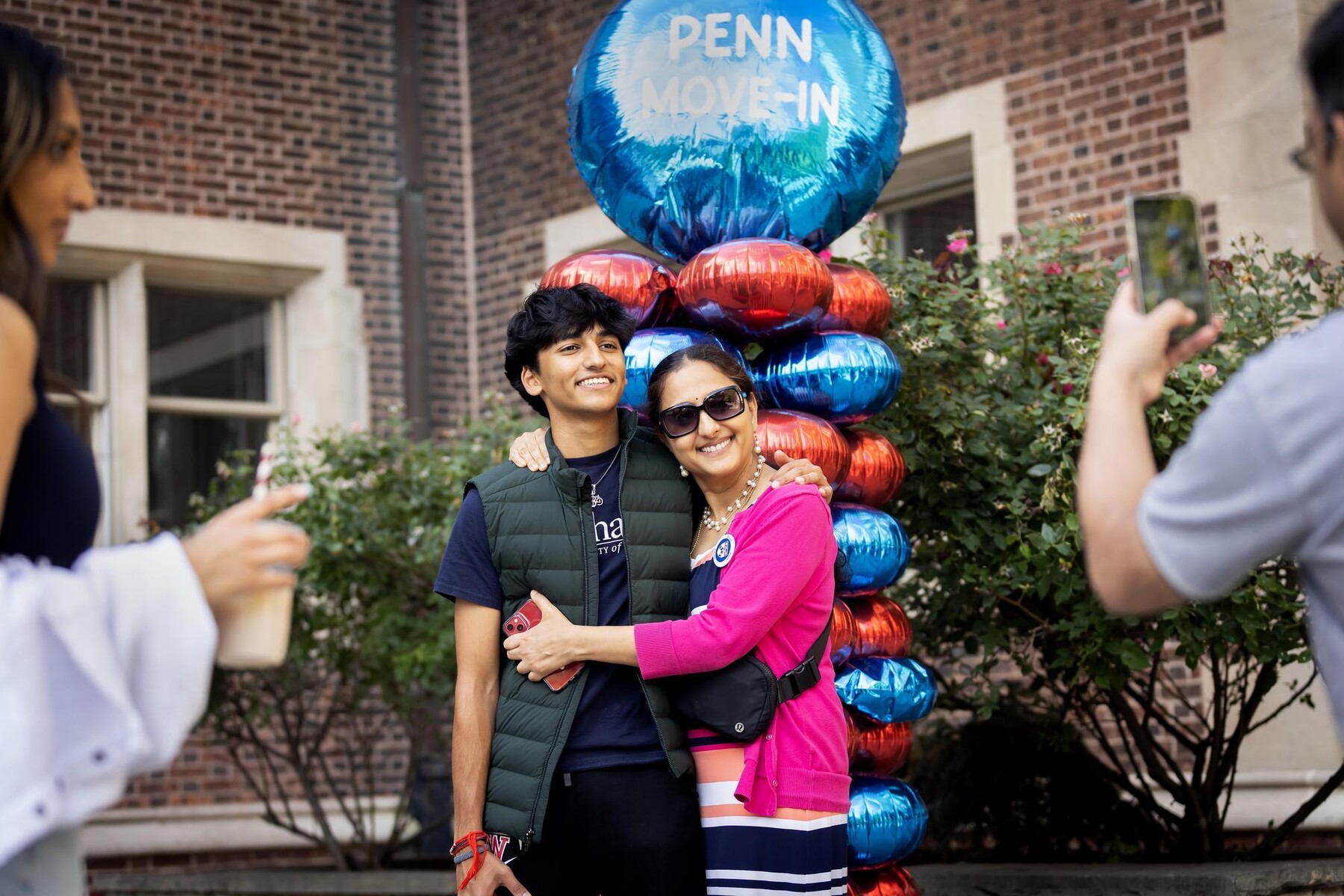 A parent hugging their student and having their photo taken under a ballon that reads PENN MOVE IN.