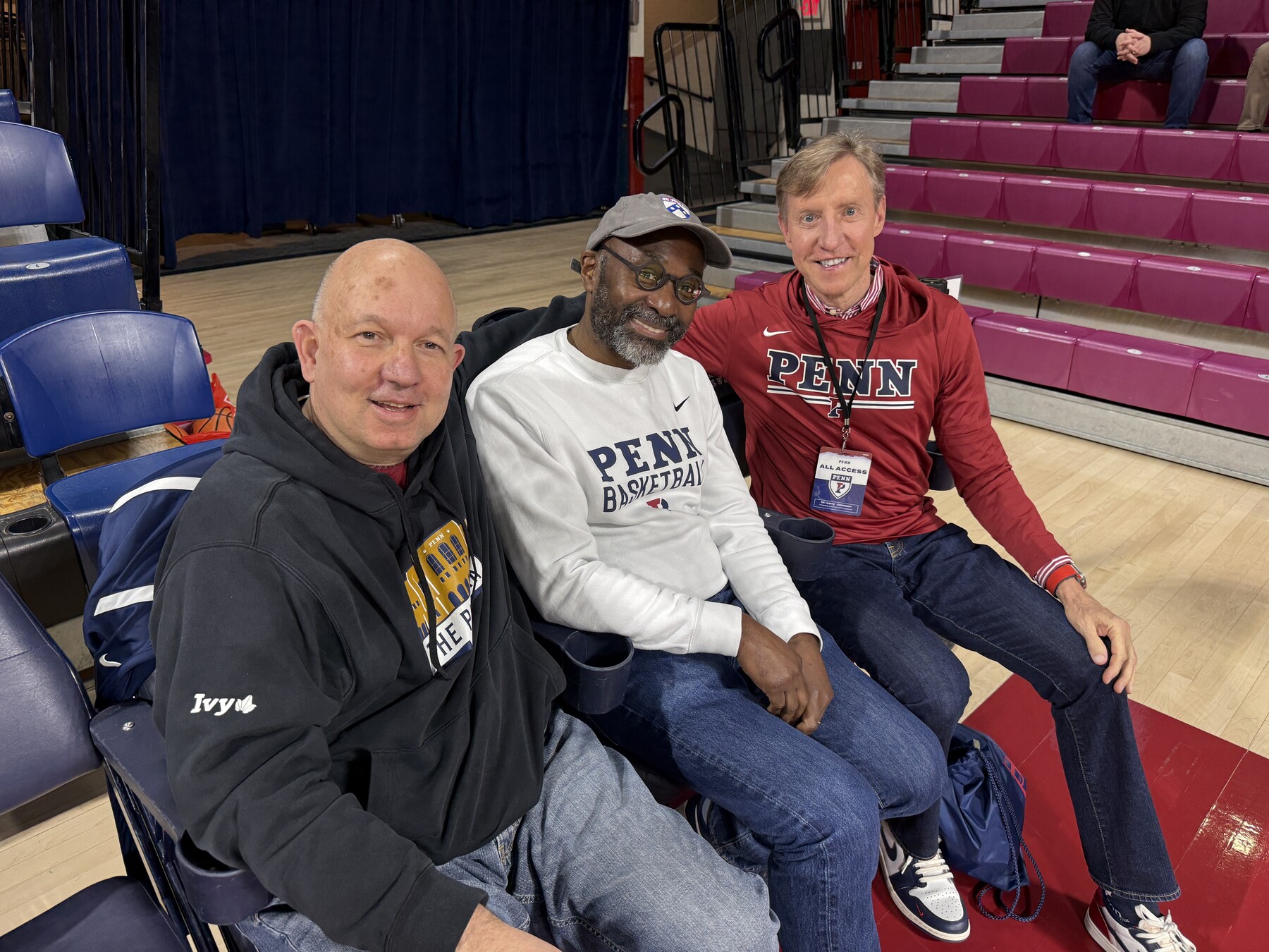 J. Larry Jameson and John L. Jackson Jr. and another person seated on the sidelines of a Penn basketball game.