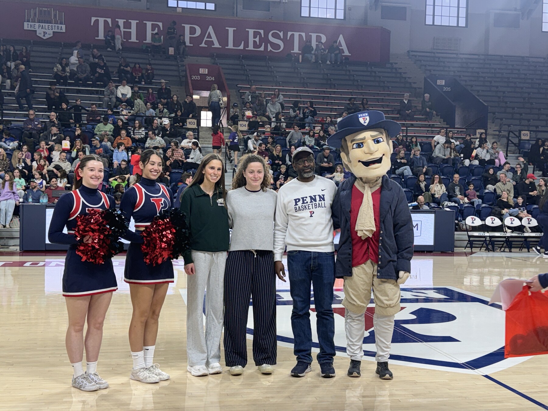 John L. Jackson Jr., two cheerleaders and the Quaker mascot on court at a Penn basketball game.