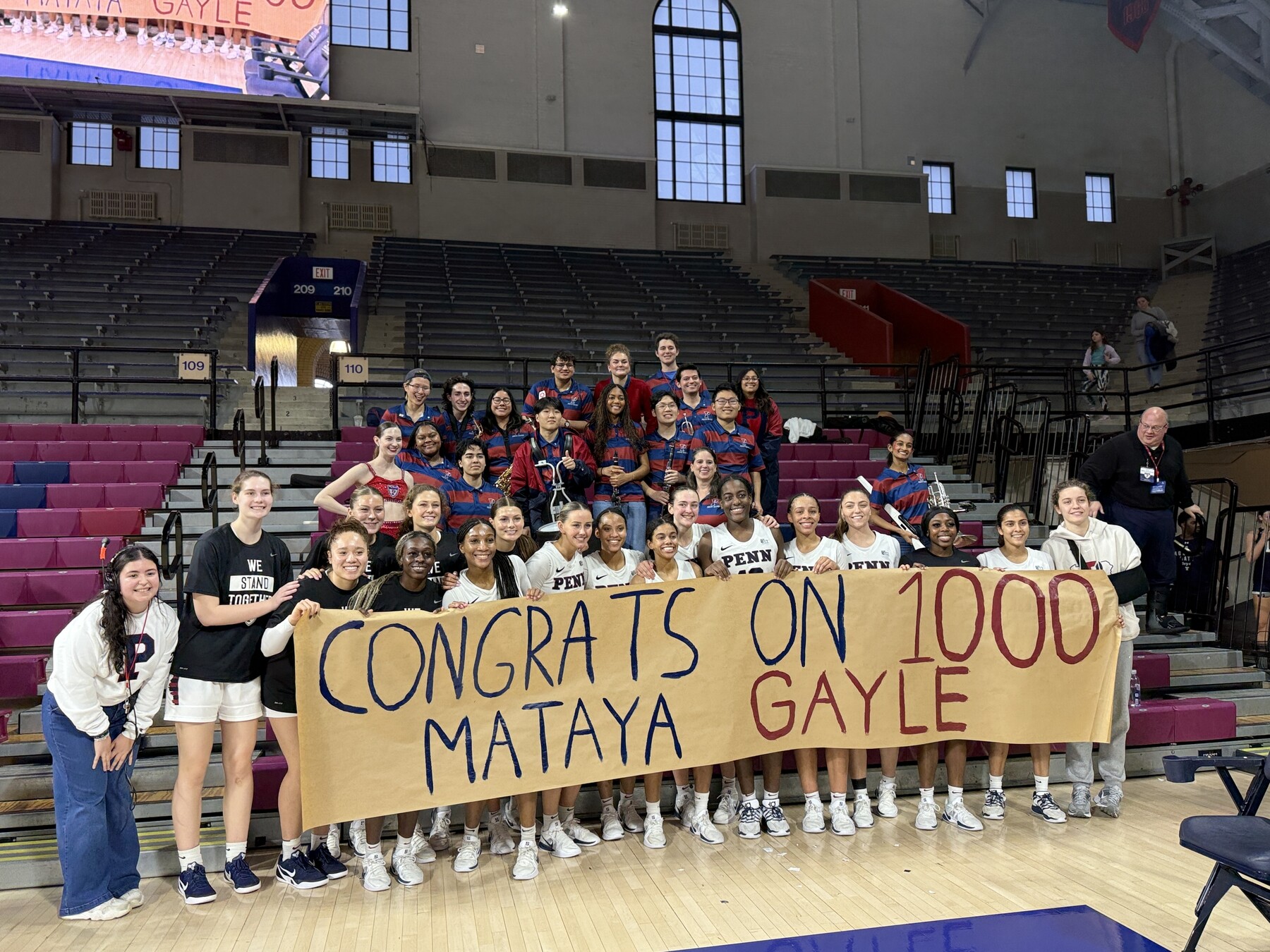 The Penn women’s basketball team holding a sign that reads CONGRATS ON 1000 MATAYA GAYLE.