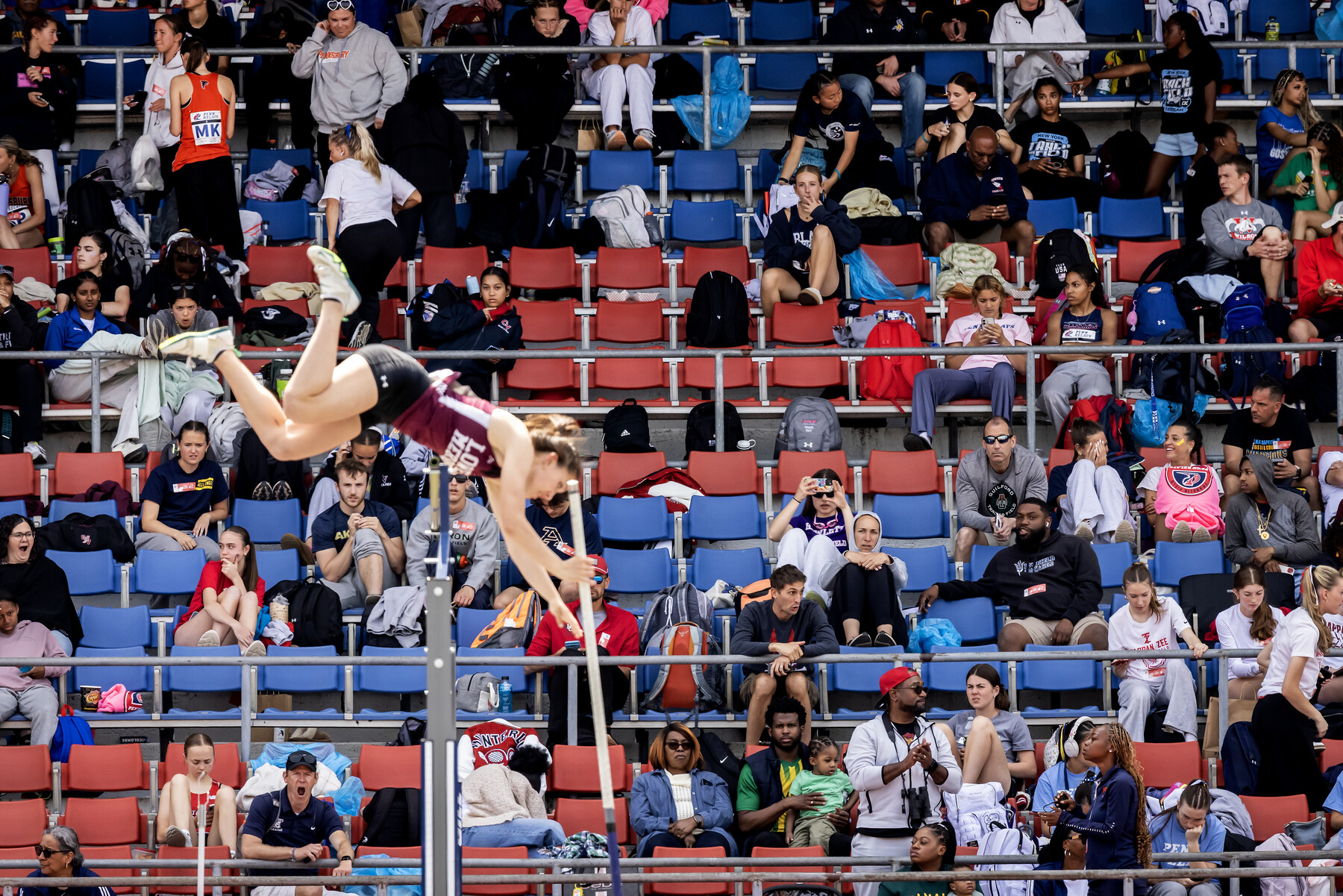 A pole vaulter in the air and the crowd in the bleachers behind them.