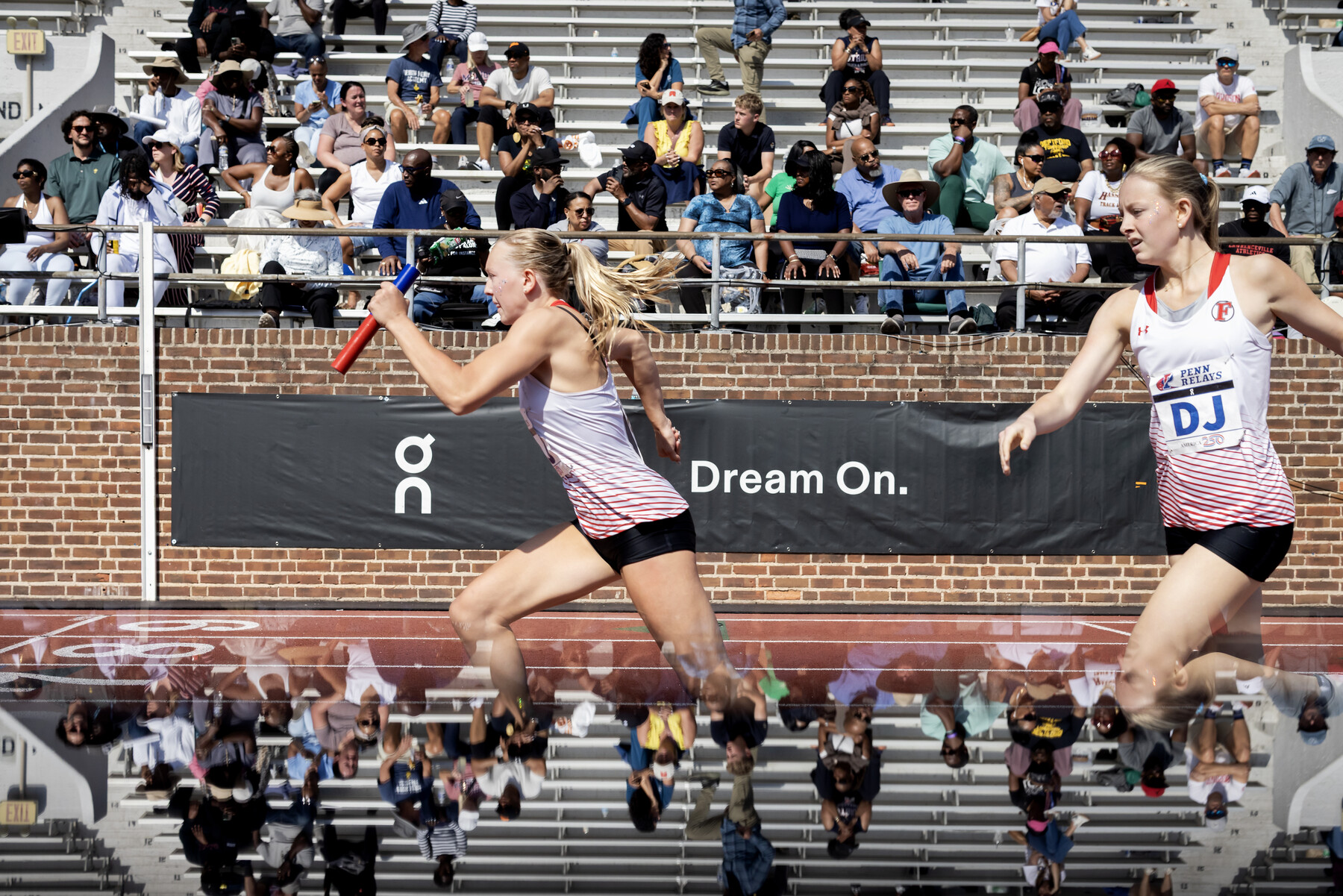 Two runners during a baton handoff at the Penn Relays on Franklin Field.