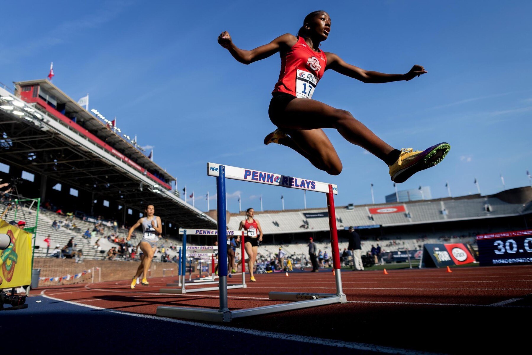 A runner jumping over a hurdle on the track at Franklin Field during the Penn Relays.