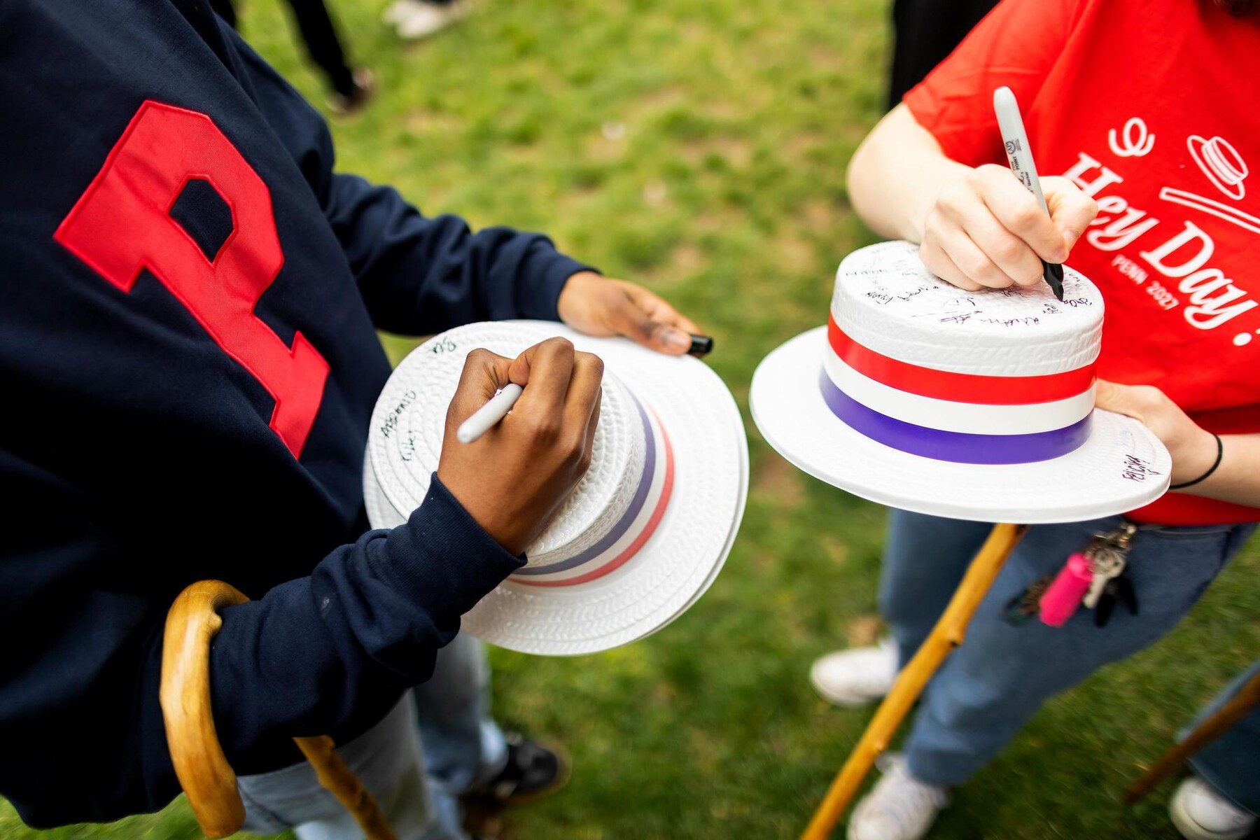 Two Class of 2027 students signing hats with Sharpies on Hey Day.