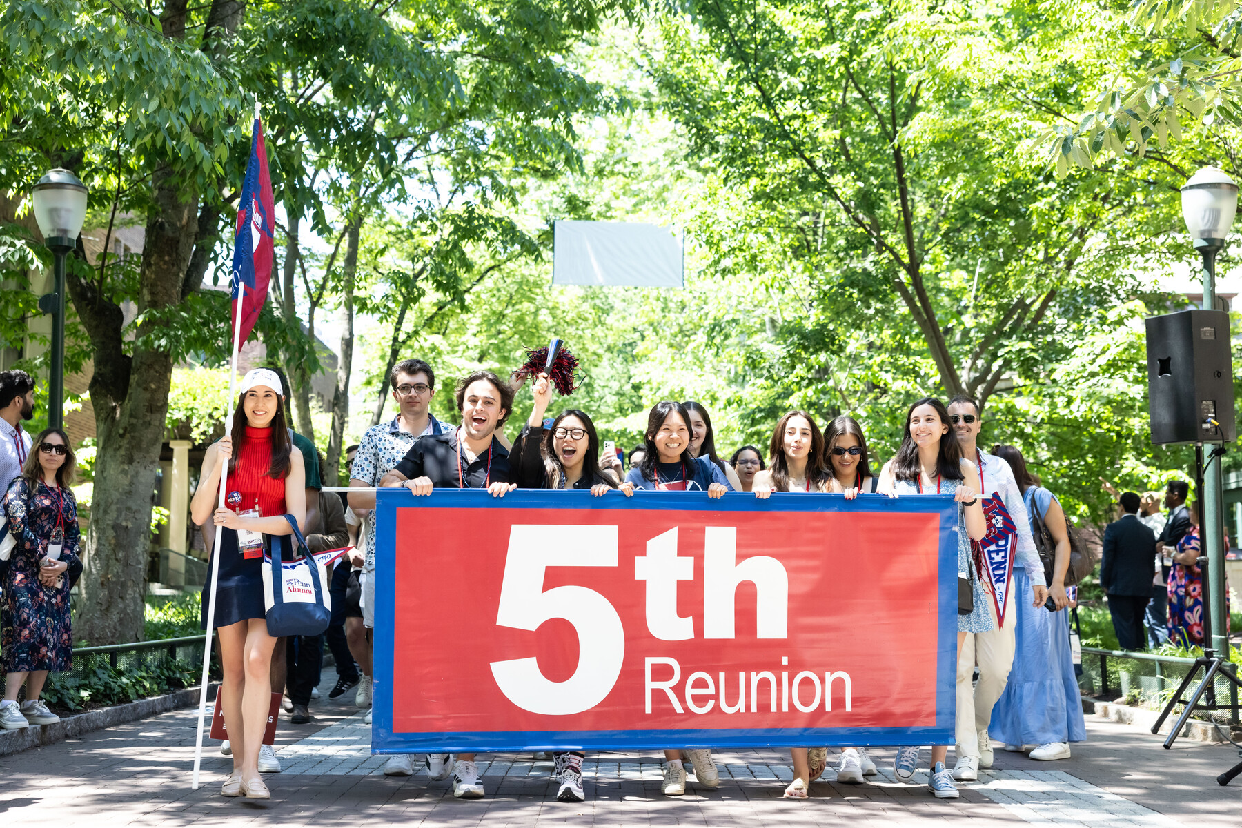 Penn alum celebrating their 5th reunion behind a banner on locust walk