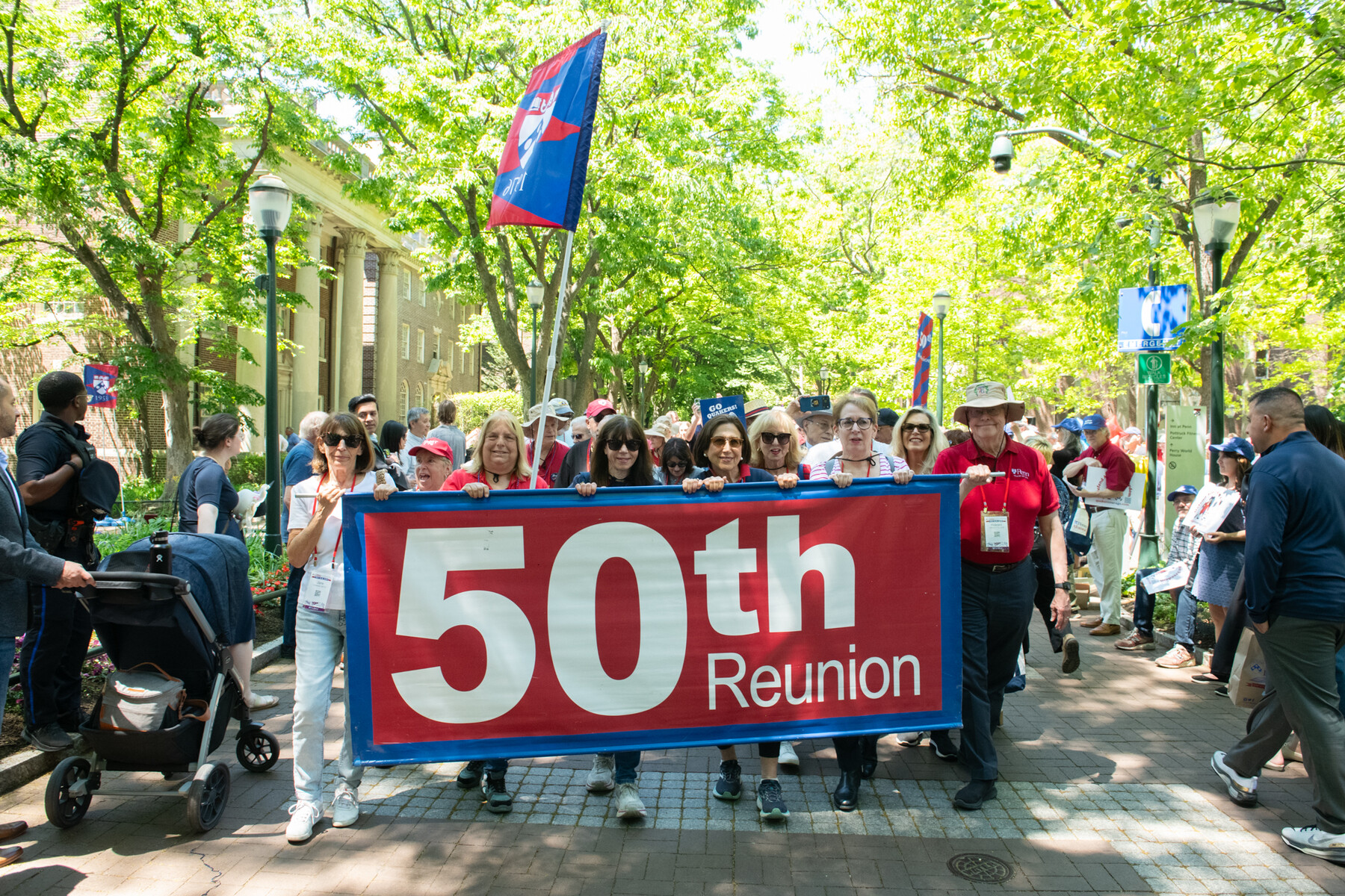 Penn alum on locust walk behind a banner celebrating their 50th reunion.