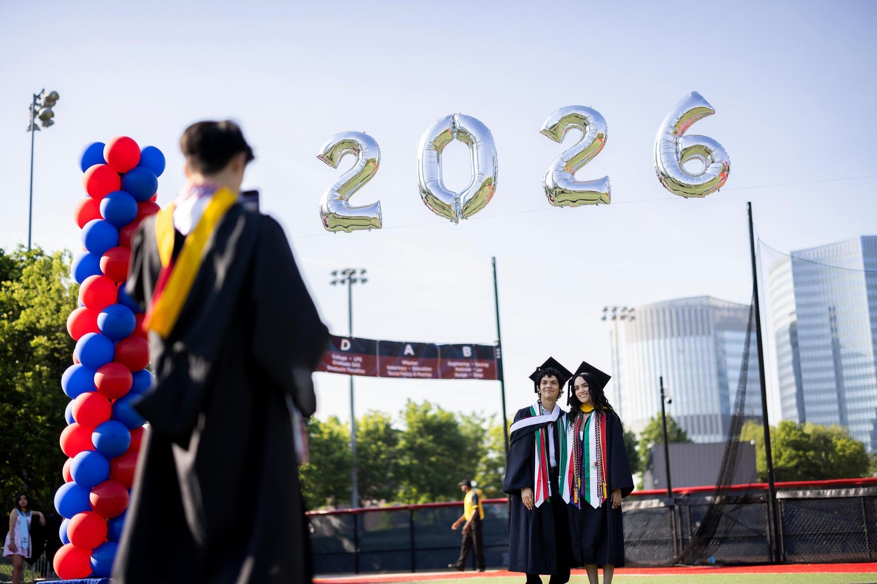 Two people having their photo taken under a 2026 balloon display before commencement.